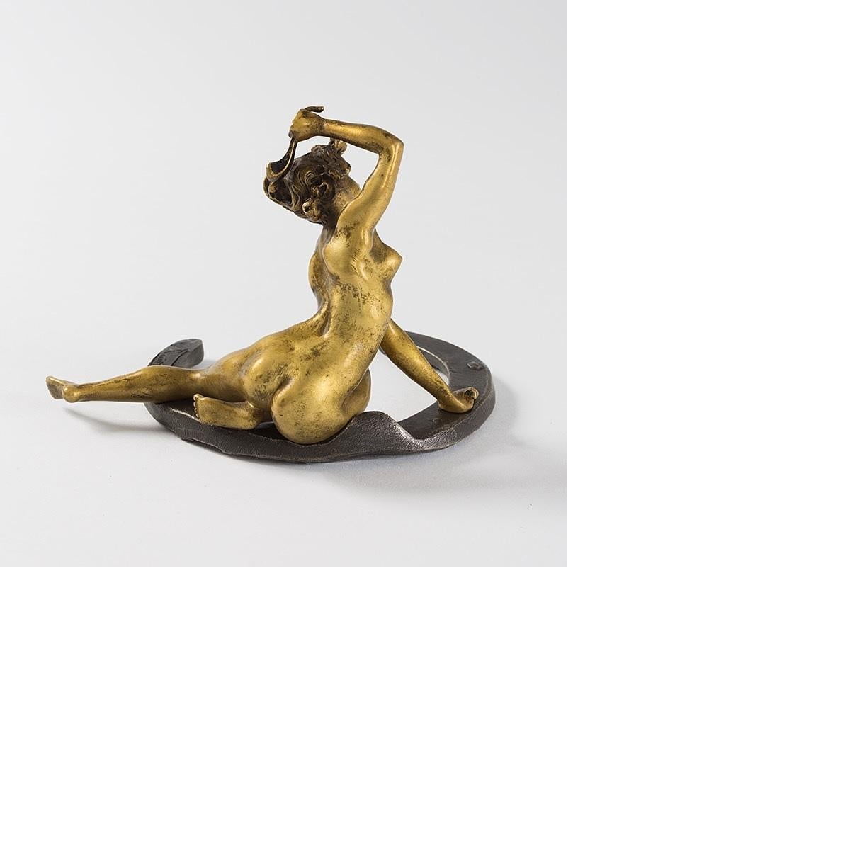 A French Art Nouveau gilt and patinated bronze figural sculpture, titled Porte-bonheure a la muse ou La Chance, by Georges Récipon (1860-1920). The desk weight is modeled as a female nude hammering nails into a horseshoe, circa 1900.

A similar