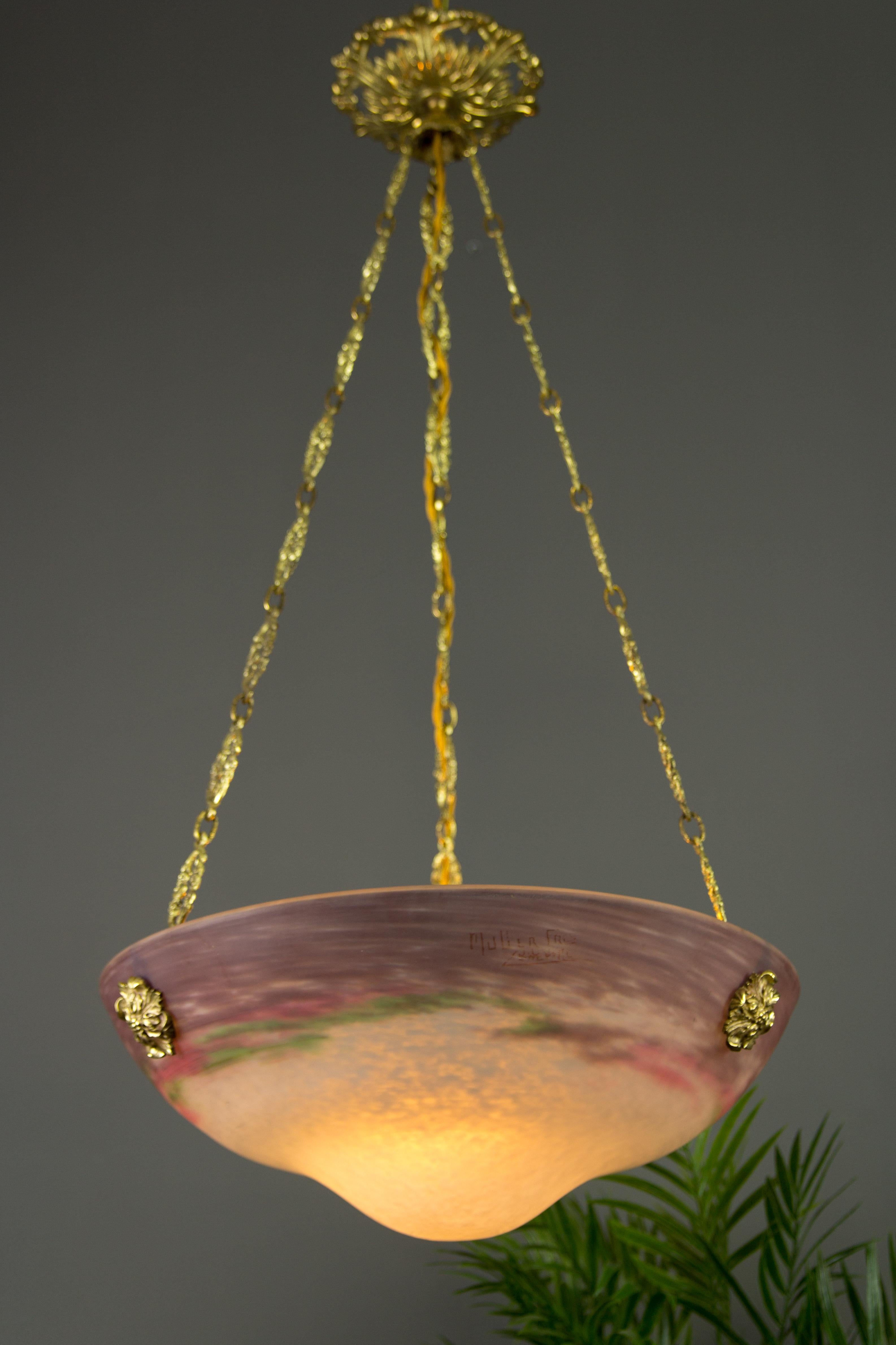 This adorable French Art Nouveau period pendant chandelier features a very unusual shaped mottled “Pâte de Verre” glass shade in white, purple, and green color, marked with Muller Frès Luneville, hung at an ornate bronze and brass fixture with one