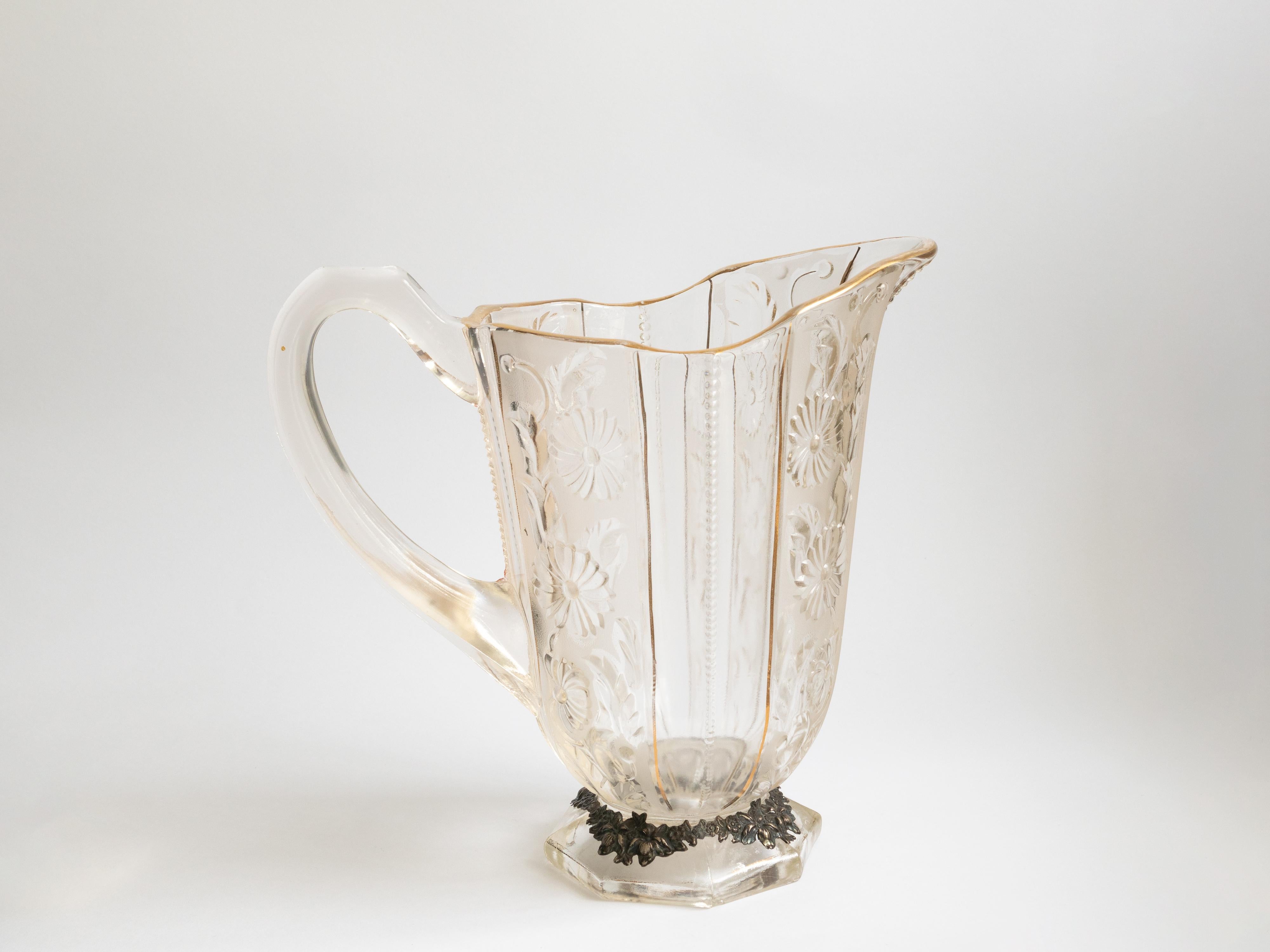 Chef-d'œuvre de l'Art nouveau fabriqué en France (1910-1921), ce pichet en verre argenté présente un corps en verre moulé transparent avec un bord sinueux orné de délicates lignes dorées. 
La base hexagonale, joliment ornée de tournesols argentés