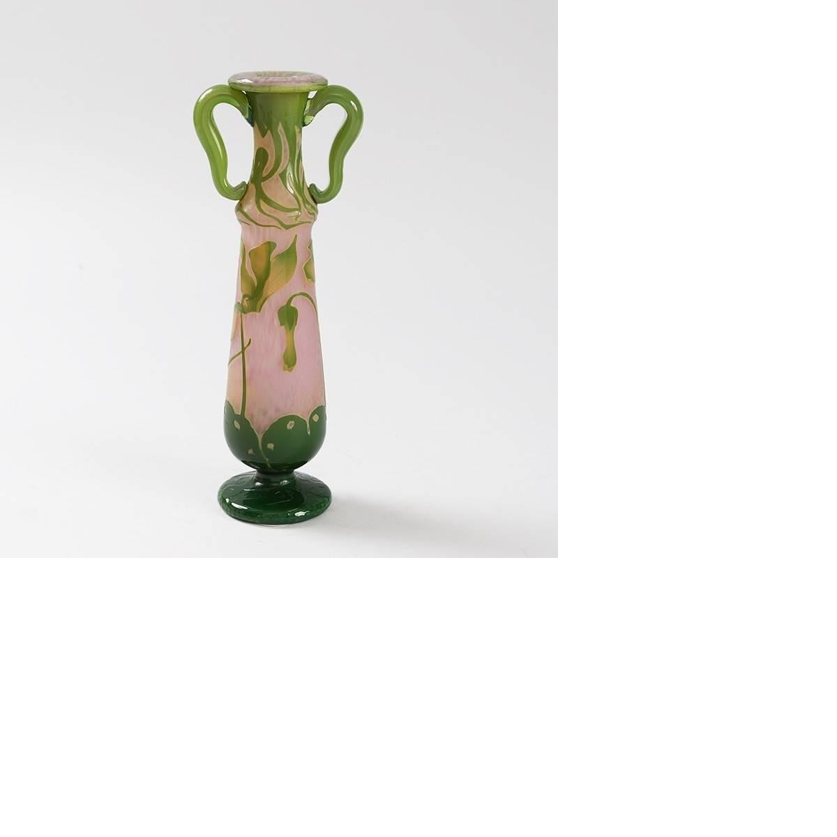 A French enameled and etched glass vase with applied handles by Daum. The vase has a pink martelé background. There is carving on the dark green footed base. It is decorated with lighter green wheel-carved flowers and vines. Additional wheel-carved