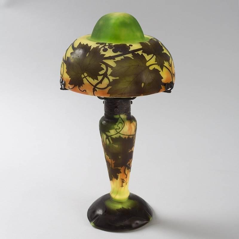 A French Art Nouveau cameo glass lamp by Daum Nancy. The lamp features grapevines, leaves and clusters of grapes, in shades of green and brown, wrapped around the shade. A decoration of carved leaves ornaments base of the lamp. The lamp culminates