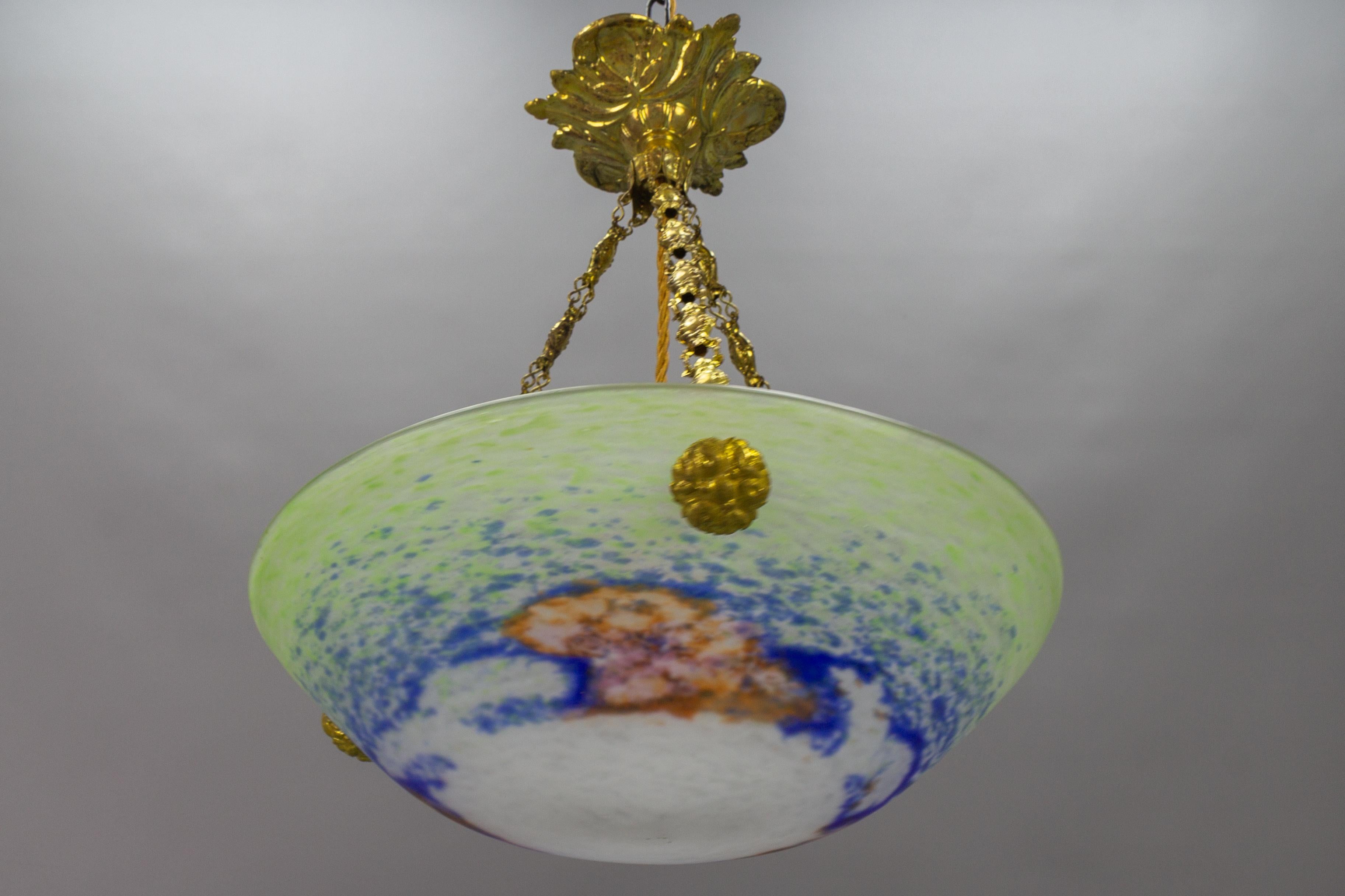 This adorable French Art Nouveau period pendant chandelier features a mottled “Pâte de Verre” art glass bowl in green, blue, and white color with orange and pink accents, attributed to Jean Noverdy, hung at an ornate brass canopy. The pendant light