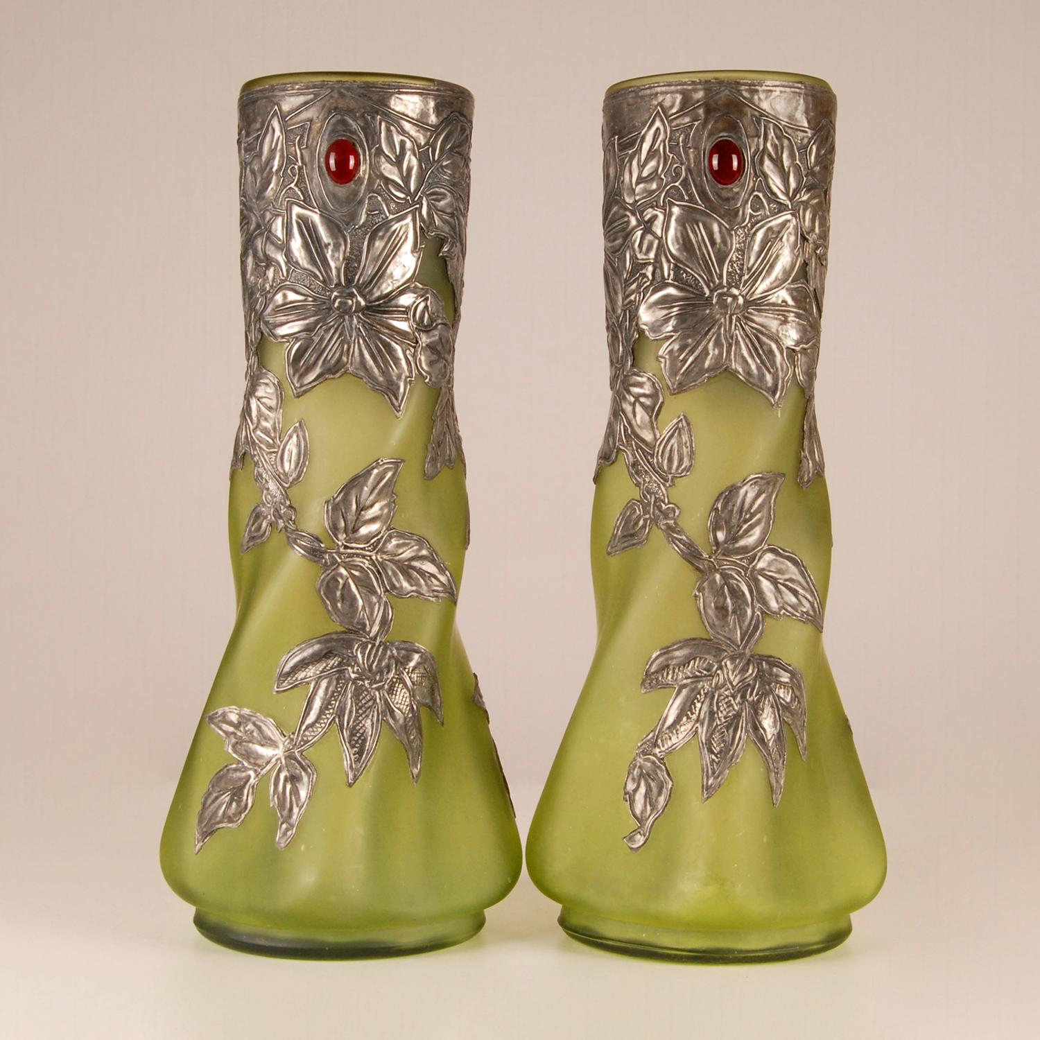 A pair French art glass pate de verre vases with pewter and glass paste stones
The vases are made of green pate de verre mounted in floral shaped silver pewter and jewelled on front and back with cabochon cut glass paste stones
Design: In the