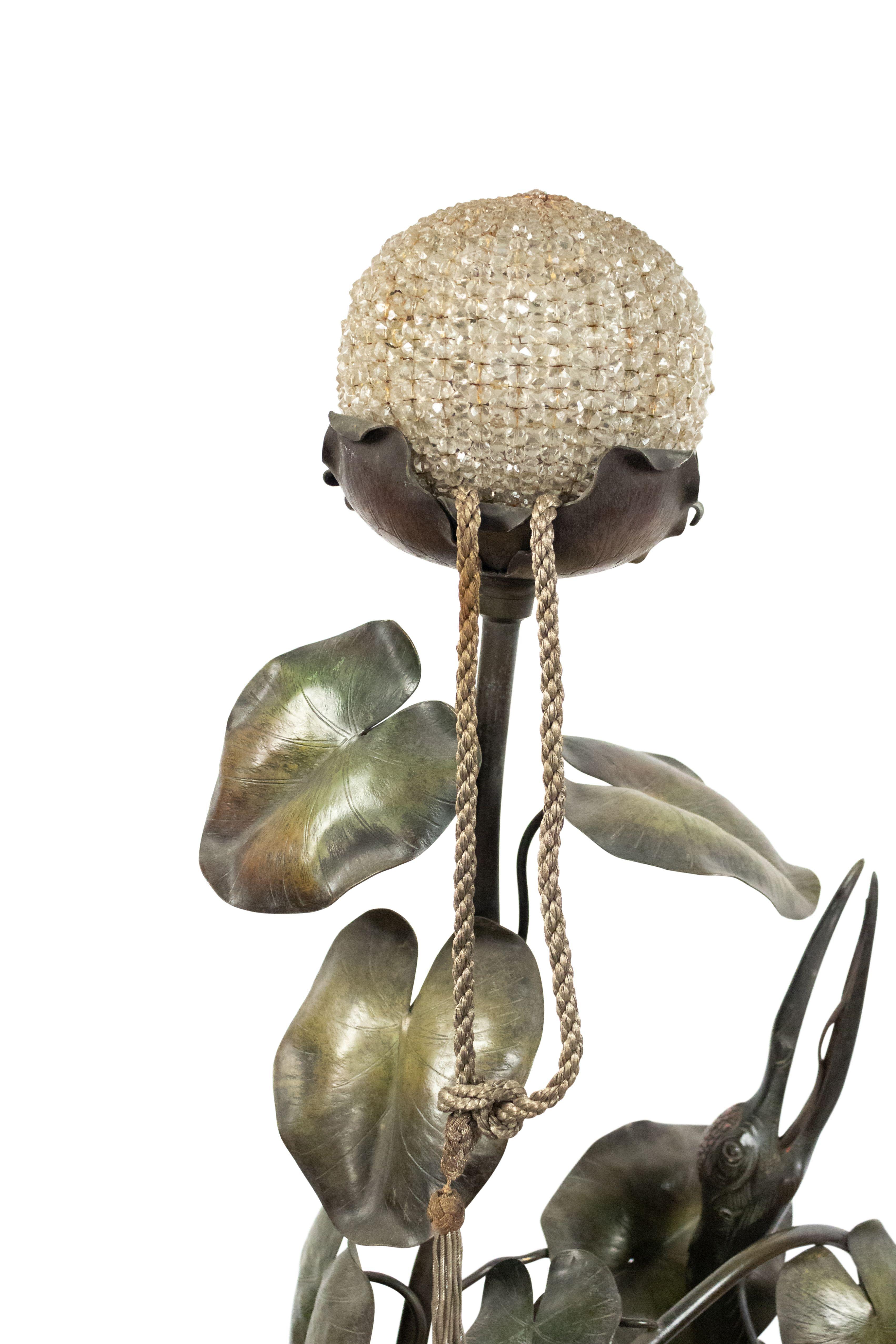 French Art Nouveau floor lamp of a large heron figure standing on and surrounded by lilly pad leaves with several crystal bead encased lights at base and on top.
     