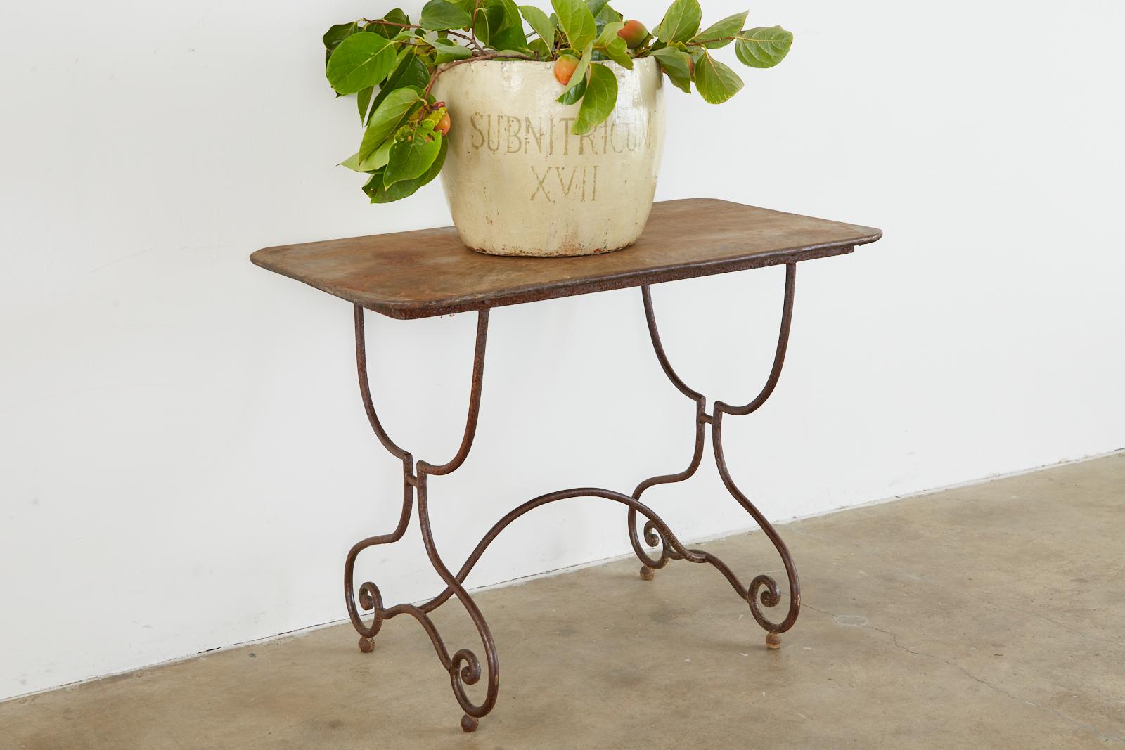 Charming French Art Nouveau bistro or cafe dining table crafted from wrought iron. Features a thick iron trestle style base with scrolled legs ending with ball feet. The legs are conjoined by a curved stretcher. Topped with a rectangular iron