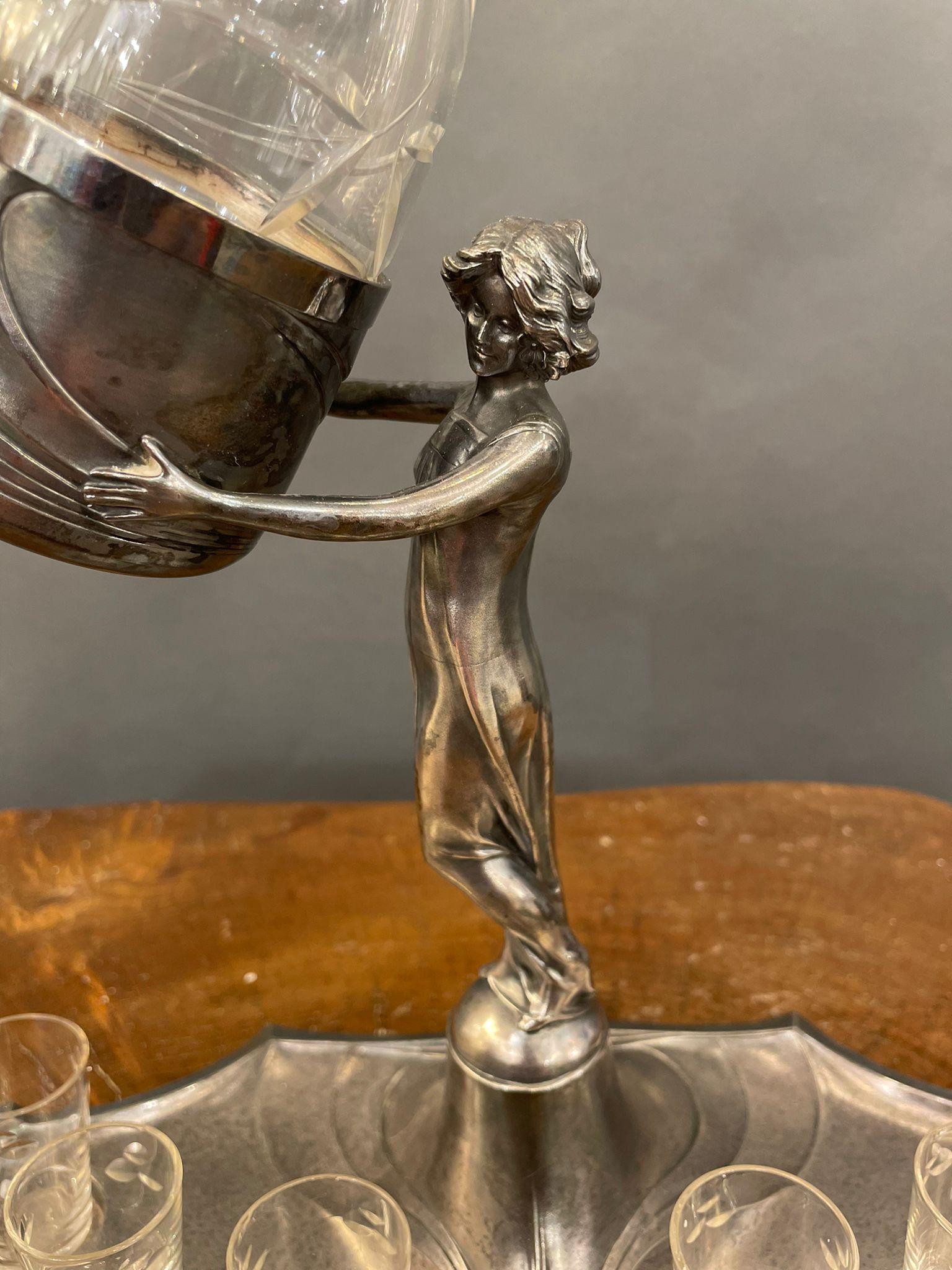 French vintage Art Nouveau nicest liquor set in silver plate with a sculptured female figurine.
Silver plate tray with six small glasses, in the middle of the tray stands a sculptured female figurine wearing a long dress holding the decanter with
