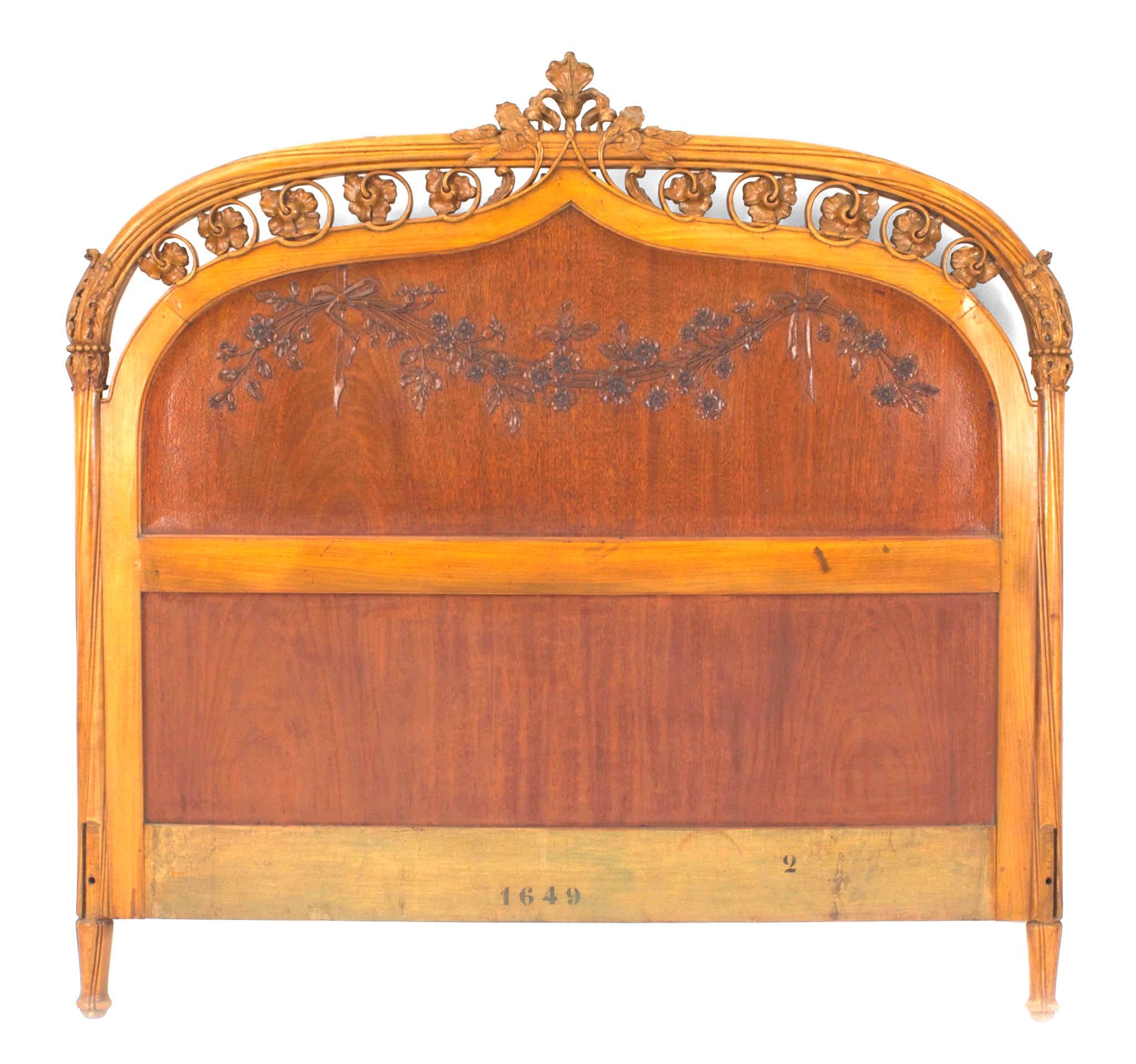 French Art Nouveau maple full size headboard having a carved and filigree floral and vine design carved edge framing a dark stained panel with a floral swag carved relief (includes headboard only)
