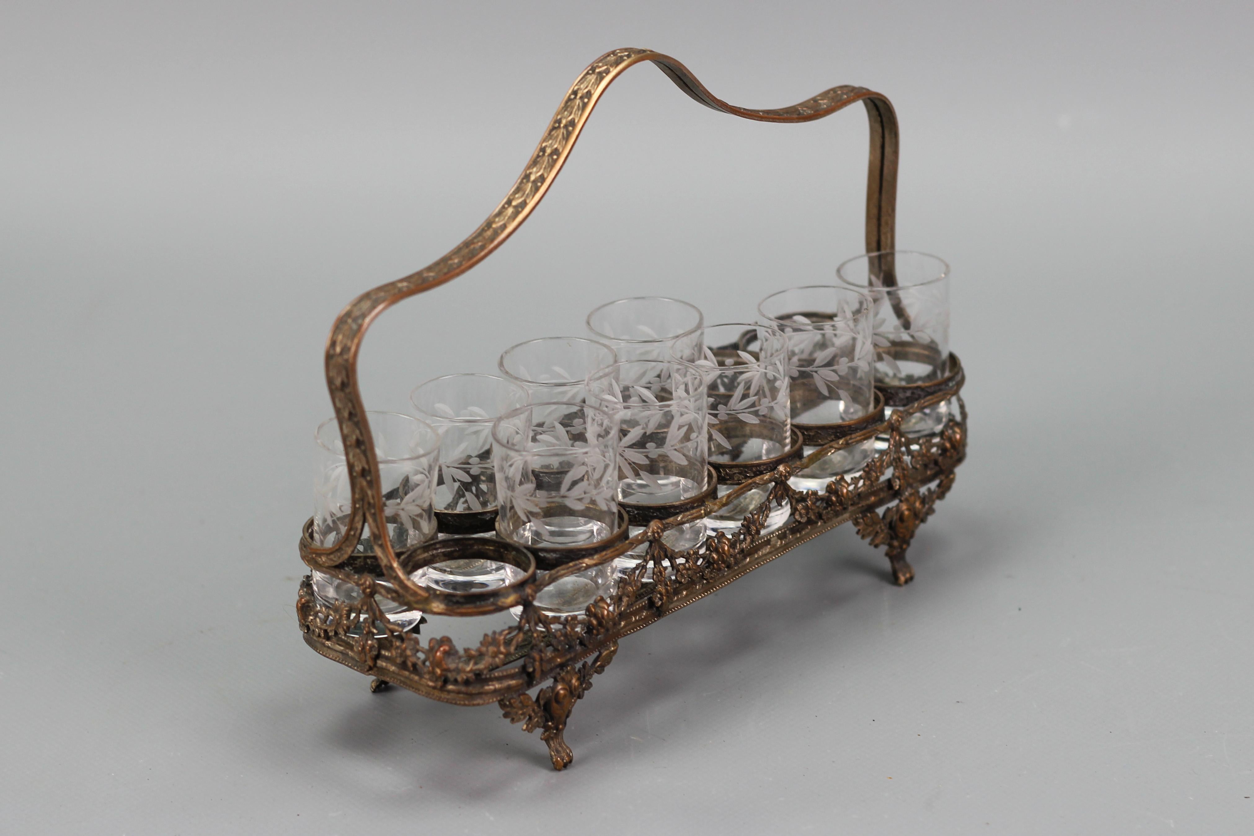 Antique French Art Nouveau nine glasses and brass basket serving set, ca. 1920.
This exquisite Art Nouveau serving set features nine clear glass liqueur or shot glasses with cut leaf decors and a brass basket with a place for twelve glasses. The