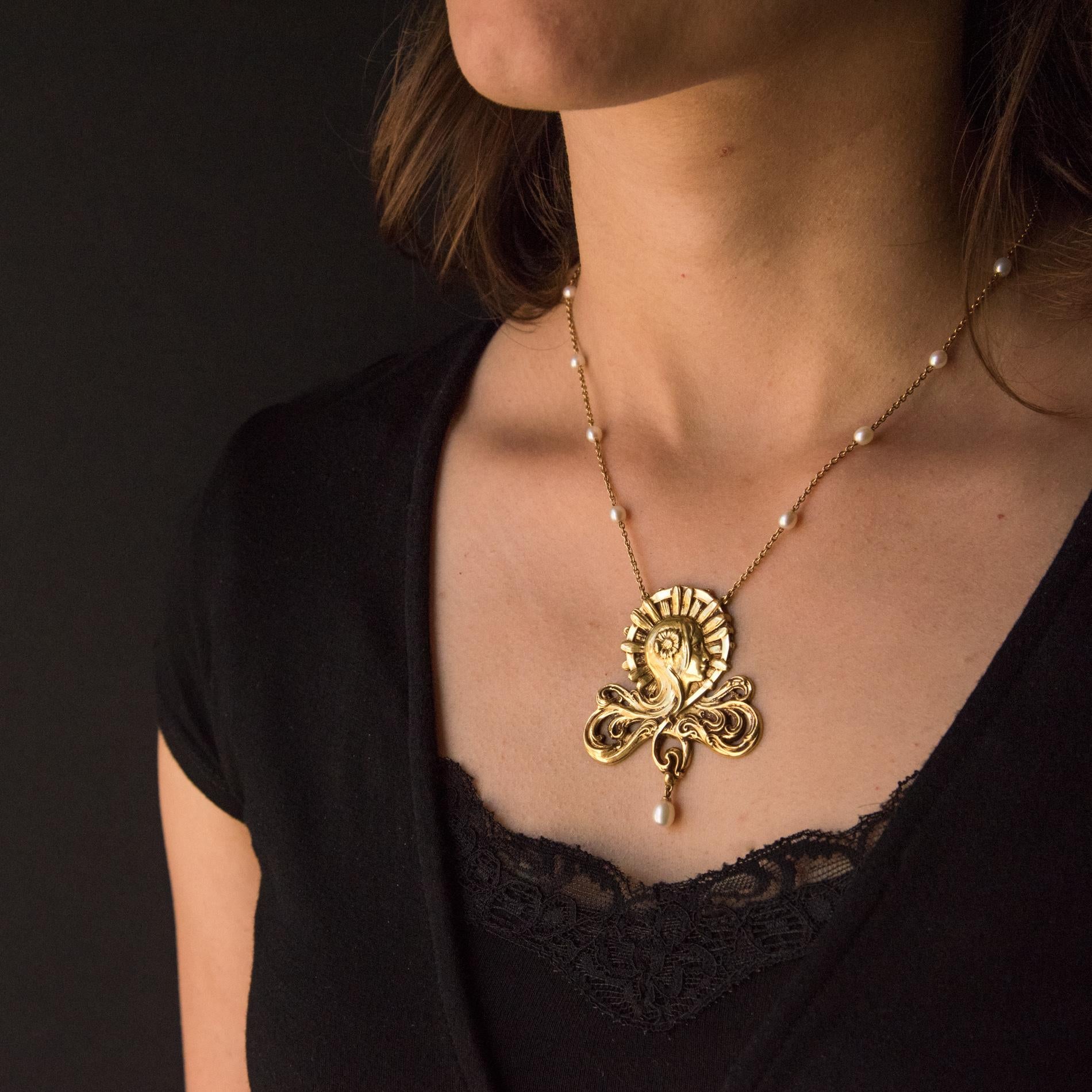Baume Kreation - Einzigartiges Stück.
Halskette aus 18 Karat Gelbgold, Adlerkopfpunze. 
Sie zeigt den Kopf einer Frau, deren Haare in ein durchbrochenes, darunter eingraviertes Muster übergehen. Sie trägt eine goldene Blume in ihrem Haar.