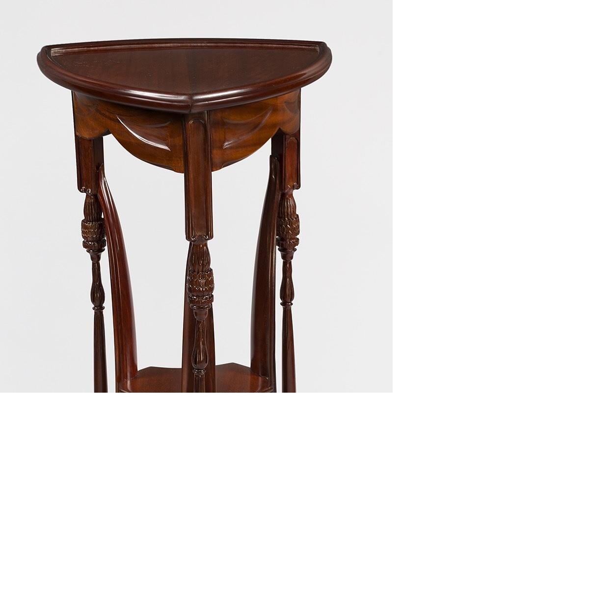 A French Art Nouveau carved mahogany three-tiered pedestal by Louis Majorelle. This piece features a triangular top with a molded gallery that sits on raised foliate carved legs with three conjoining buttresses and two shelves, circa 1900. 

This