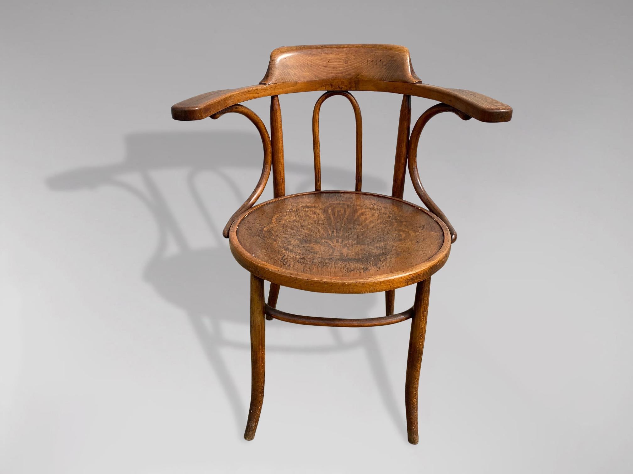 Ein Bugholzsessel des frühen 20. Jahrhunderts in gutem Originalzustand, hergestellt von Thonet in Österreich. Geprägter Sitz mit Rücken- und Armlehnen, gestützt durch geschwungene Streben. Der Sitz ruht auf sanft geschwungenen Beinen, die durch eine