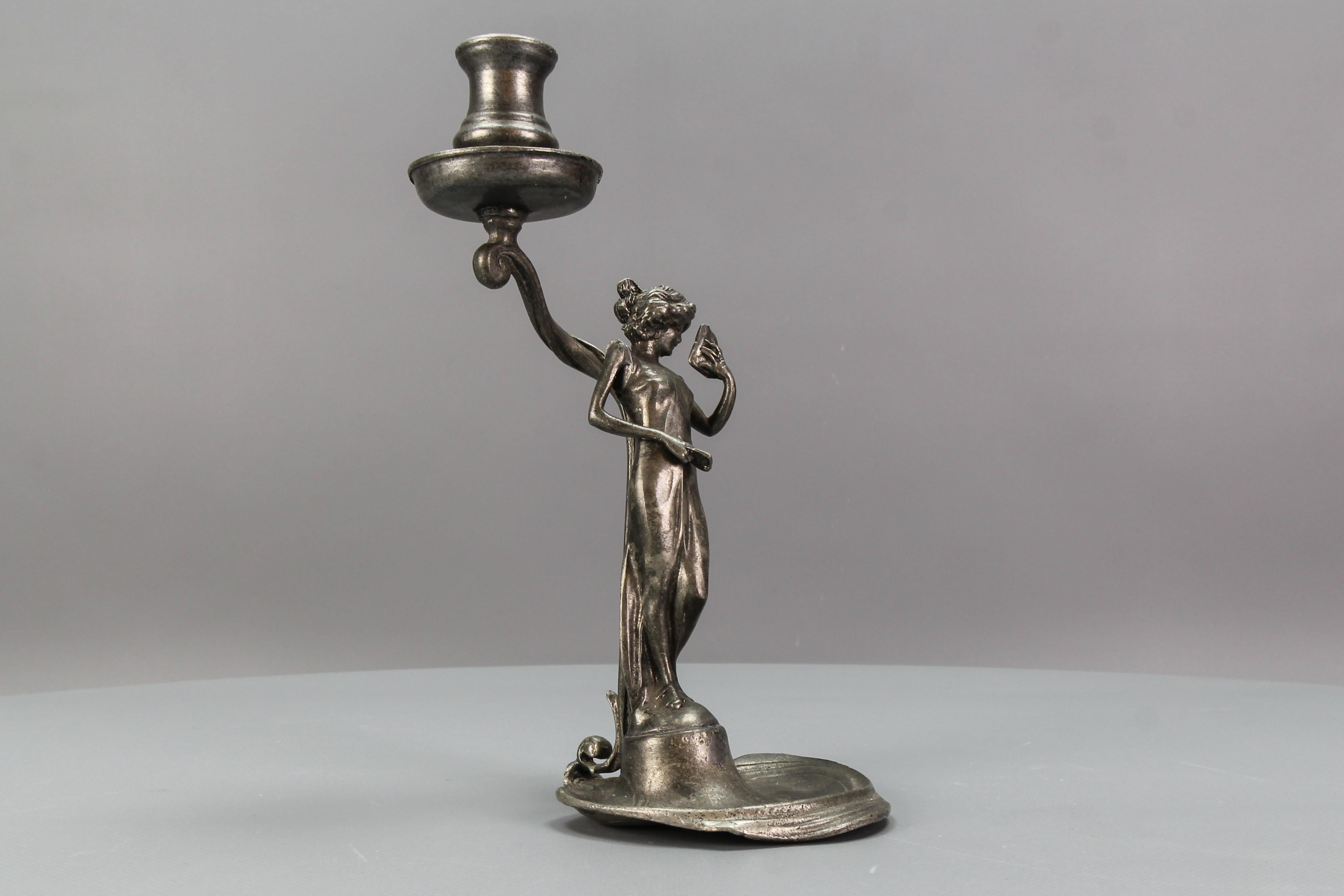 French Art Nouveau style pewter candlestick with a sculpture of a lady, from circa 1920.
An elegant Art Nouveau candle holder depicting a figure of a young and adorable lady, looking in a mirror that she is holding in one hand.
In good condition