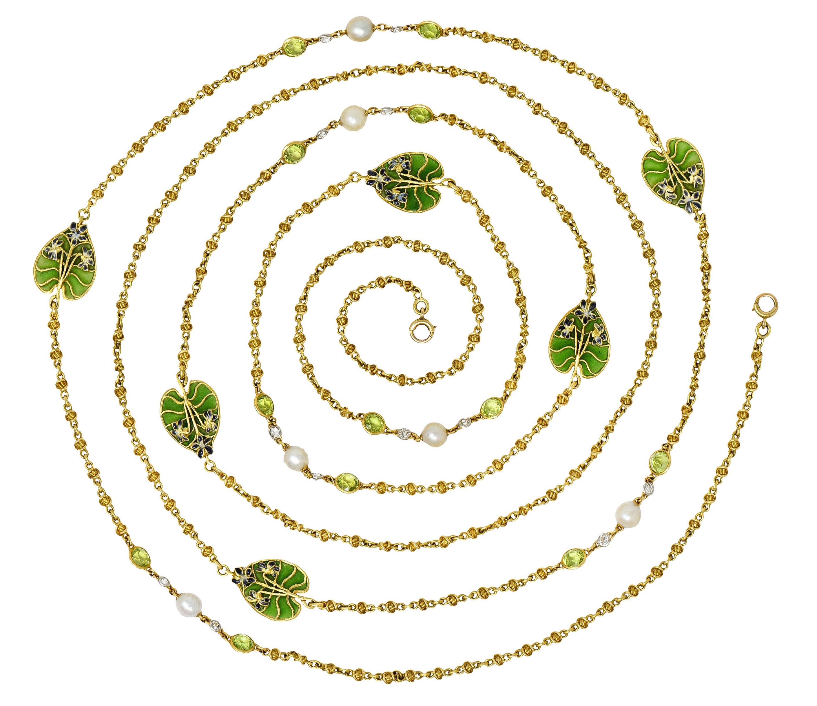 Lange Kette aus gedrehten Gliedern mit stilisierten Seerosenblättern, die sich mit Schmucksteinen abwechseln

Die Seerosenblätter sind durchscheinend mit gelblich-grüner Plique-a-Jour-Emaille, die von violett und weiß emaillierten Blumen akzentuiert