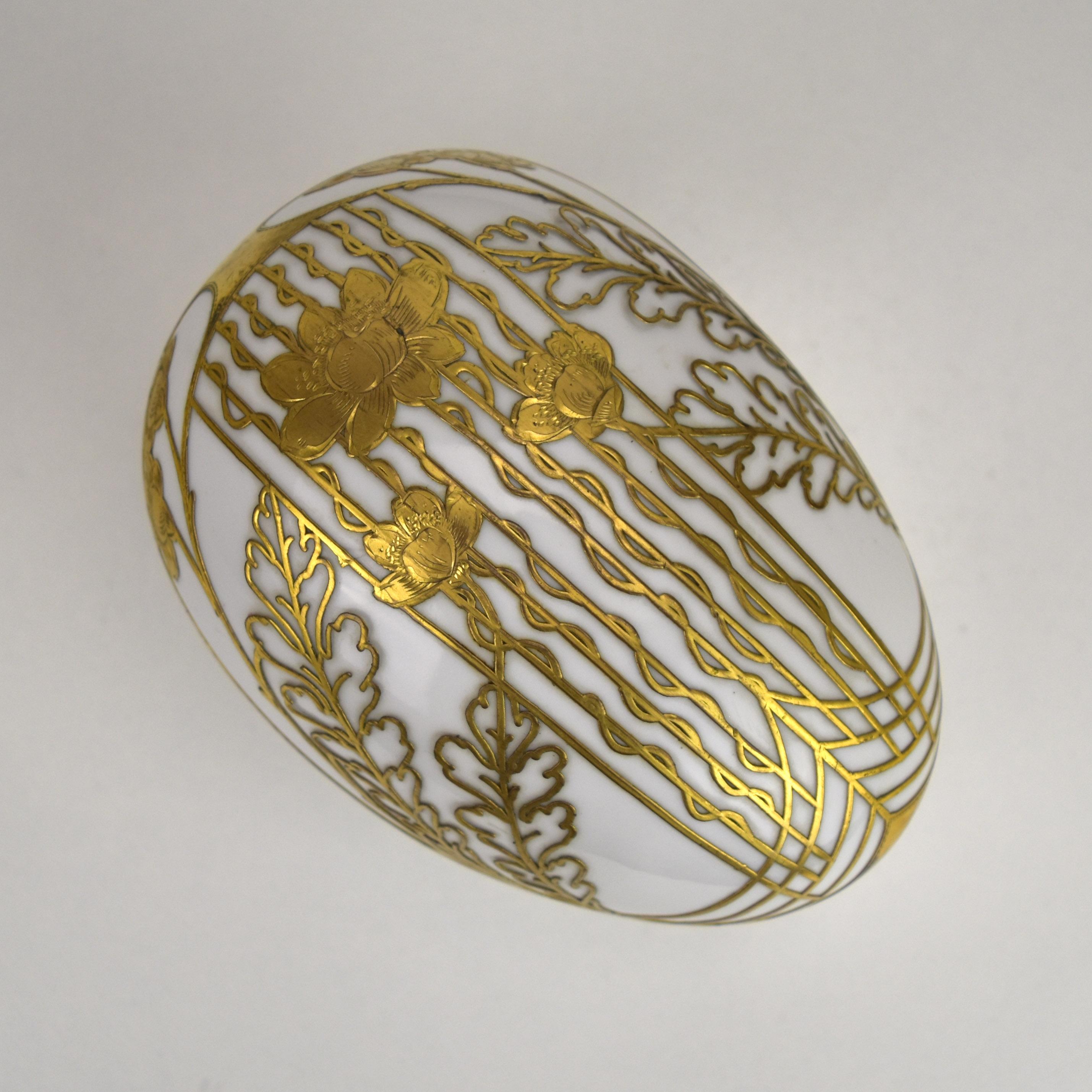 This exquisite French Art Nouveau porcelain egg box, dating to around 1900, showcases the opulent elegance of the era. The piece features a delicately crafted oval shape adorned with intricate gilt floral motifs and swirling patterns, all