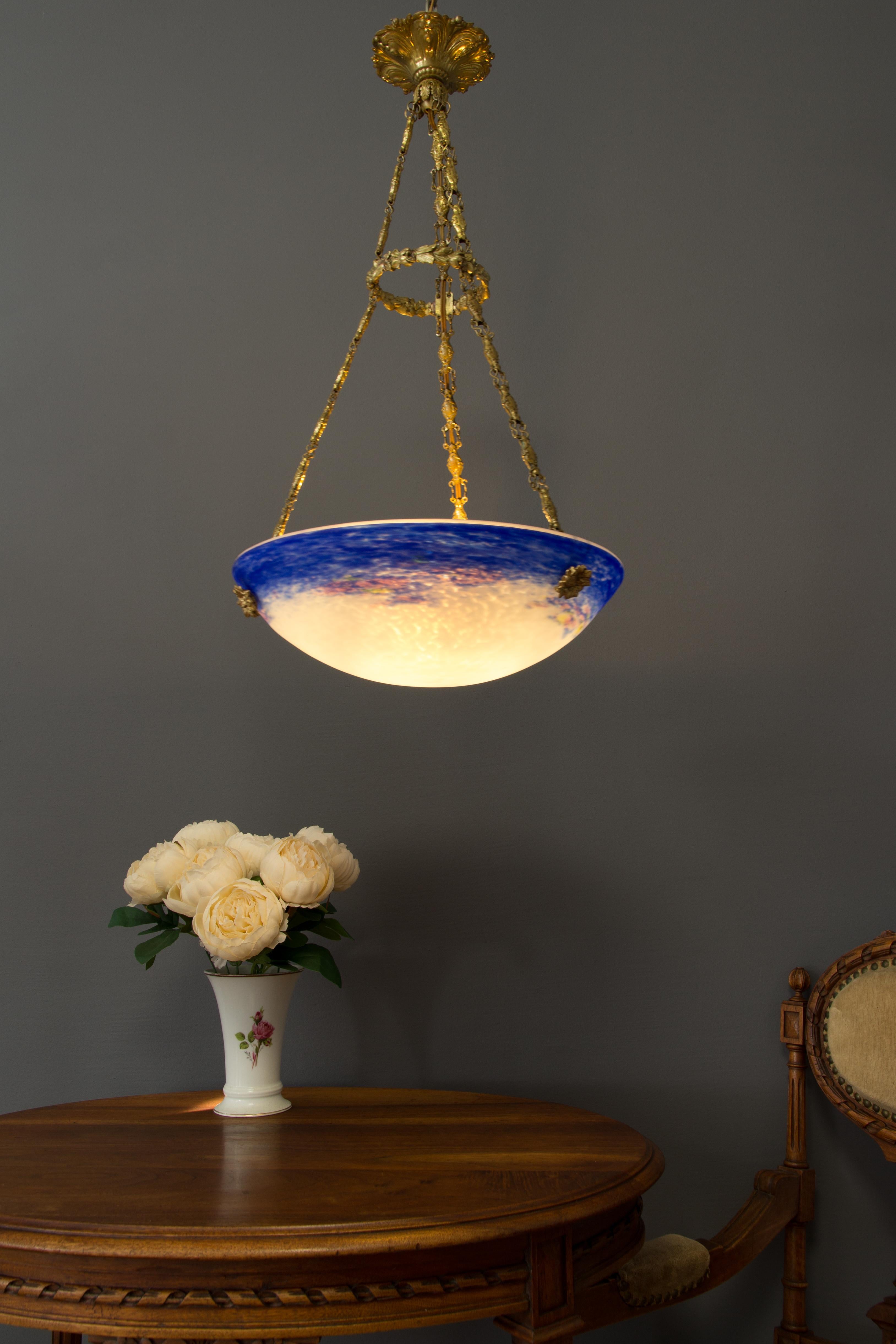 This adorable purple-blue and white French Art Nouveau period pendant chandelier features a mottled glass shade, signed” Degué”, hung at a brass and bronze fixture with one socket for an E27 light bulb.

Dimensions: diameter: 34.5 cm / 13.58 in;