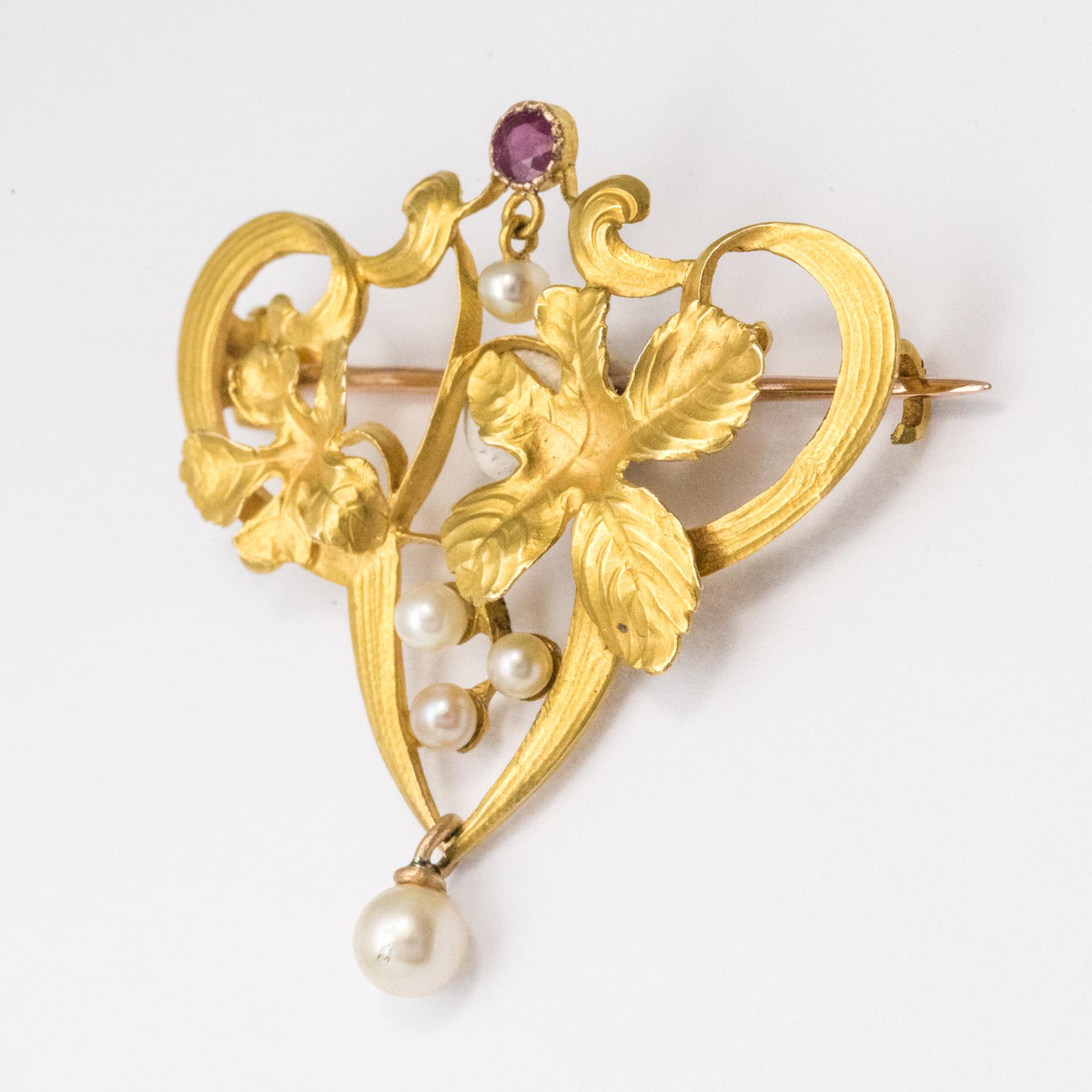 Brooch in 18 karat yellow gold, eagle's head hallmark.
A delightful Art Nouveau jewel, it represents a foliage set with three small natural pearls topped with a bezel-set ruby. Under the ruby and at the end of the brooch are set in tassel two