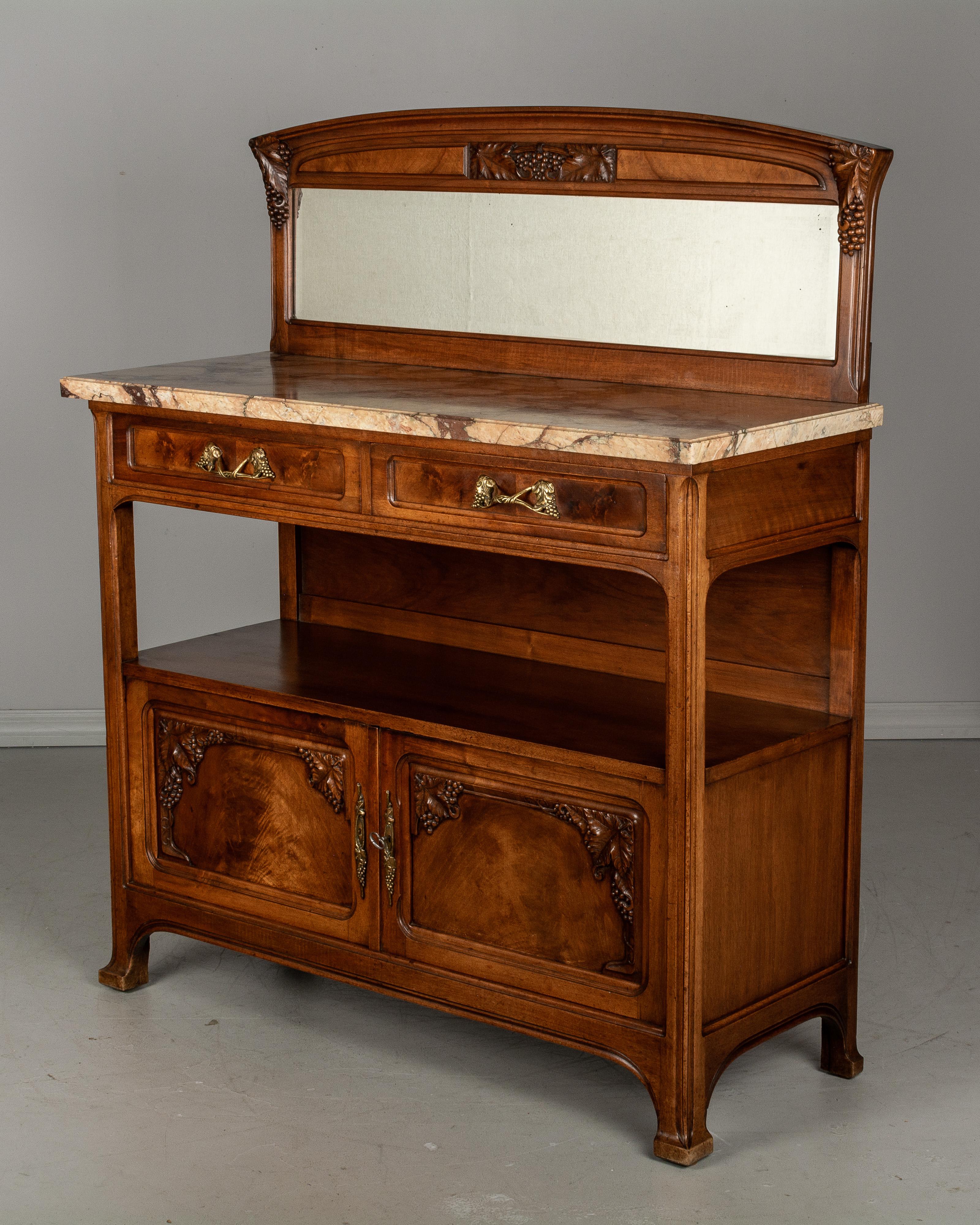 A French Art Nouveau buffet or sideboard made of solid walnut with door panels and drawers faced with beautifully patterned veneer of walnut and decorated with hand carved grape clusters. Two dovetailed drawers and two doors below an open shelf.