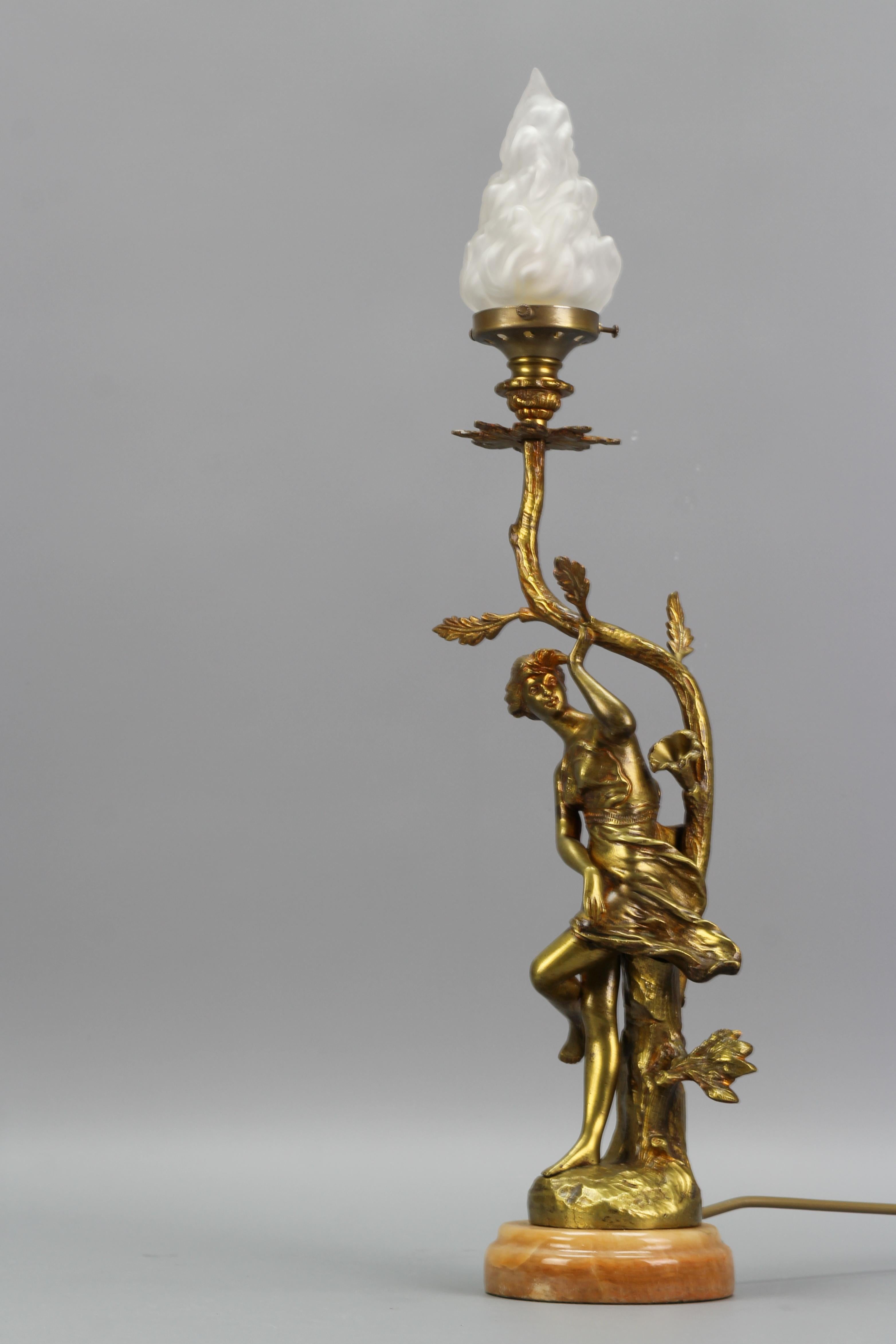 French Art Nouveau Style bronze, white glass, and onyx figural table lamp from circa the 1930s.
A beautiful French Art Nouveau style bronze table lamp, wired for single light; flame-shaped white frosted glass lampshade with a sculptural female