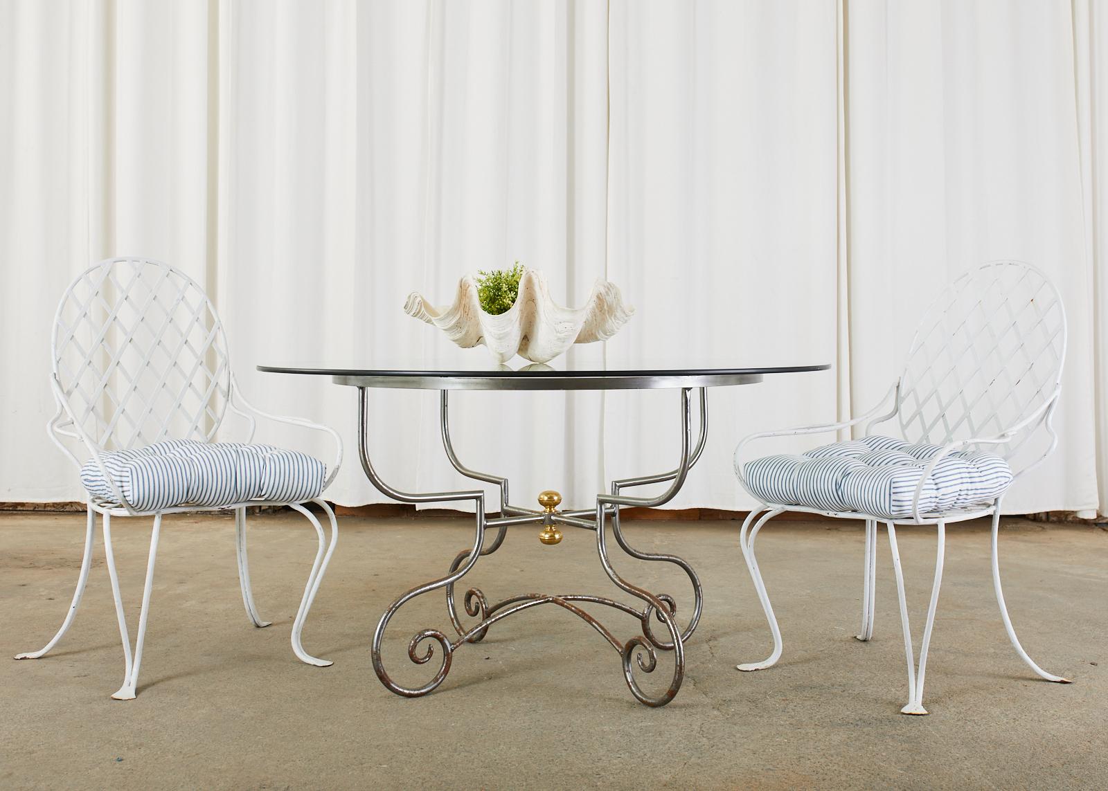 Distinctive French iron and brass dining table suitable for patio or garden. The round table features a pastry table style iron base crafted from four gracefully curved legs ending with scrolled feet. The tops of the legs are conjoined by a round