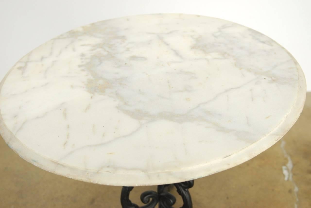 Beautiful iron and marble bistro table made in the French Art Nouveau taste. Features a cast iron painted base with decorative scrolled arms and legs. Topped with a round white piece of marble with an ogee edge. The table has a dramatic look with