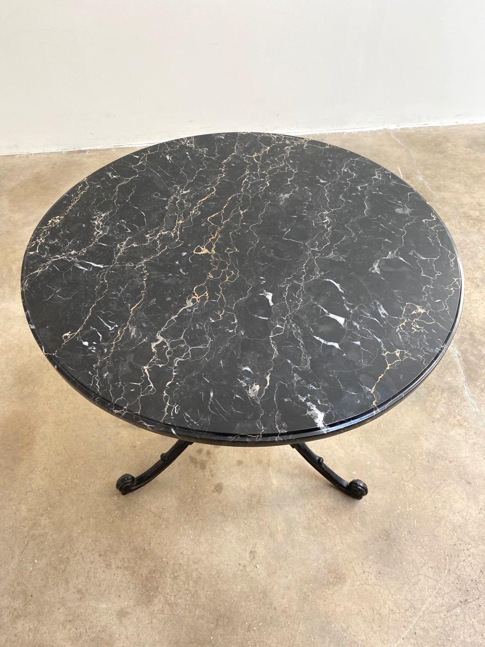 Beautiful iron and marble bistro table made in the French Art Nouveau taste. Features a cast iron painted base with decorative scrolled arms and legs. Topped with a black, gold, and white veined piece of marble with an ogee edge. 

 