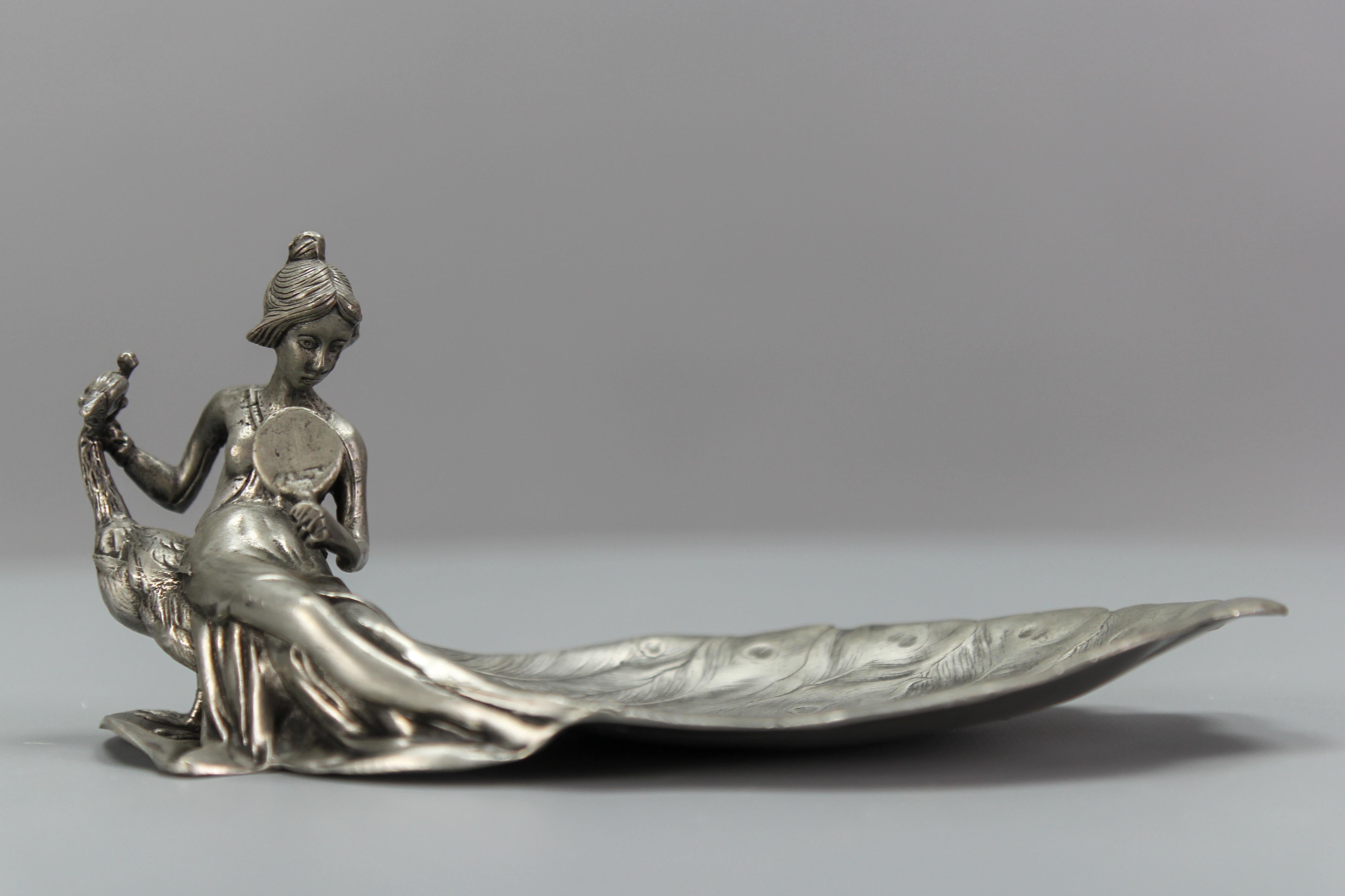 Französische Art Nouveau-Stil Zinn vide-poche oder Pin-Tablett eine Dame mit einem Pfau aus circa 1950er Jahren.
Dieses bezaubernde Karten- oder Pinnentablett, Vide-Poche, ist aus Zinn gefertigt und zeigt eine junge Dame, die in den Spiegel schaut