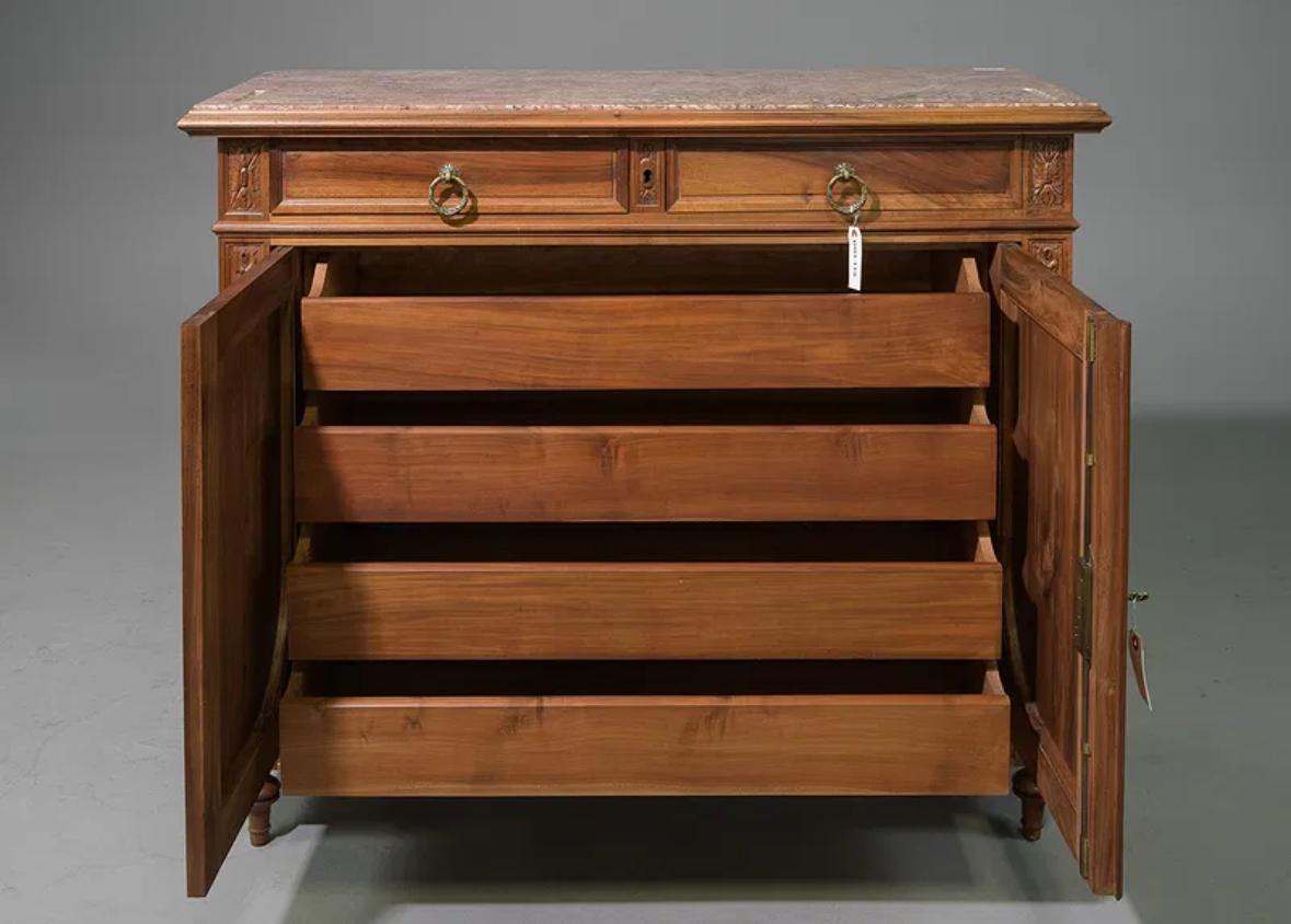 Ce buffet présente un corps en noyer finement sculpté, richement décoré de motifs floraux et feuillus, ainsi que de gracieux rubans et nœuds. Deux tiroirs supérieurs glissent en douceur au-dessus d'une paire de portes à panneaux, qui s'ouvrent pour