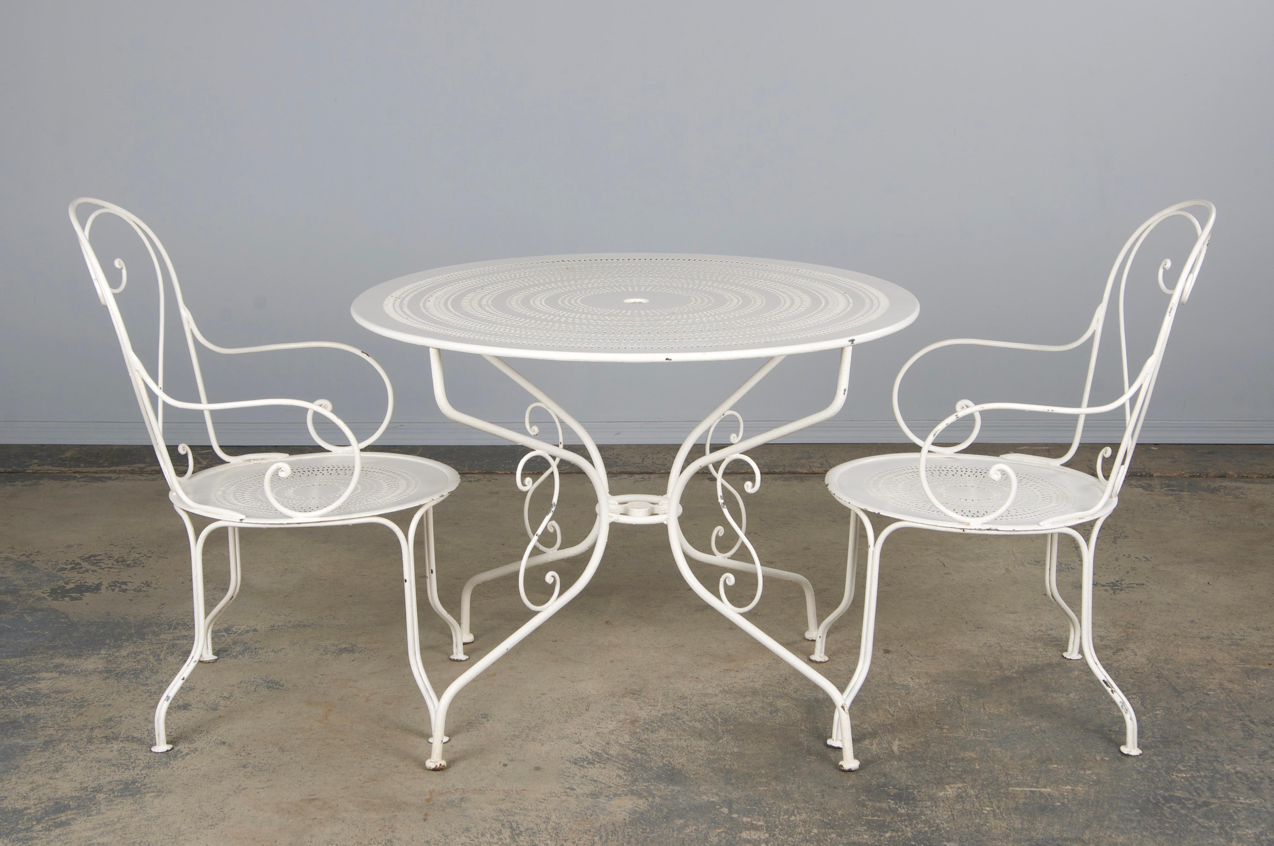 Vintage French Art Nouveau style white garden set, sourced directly from Provence, France. This set includes a round table paired with two matching armchairs, all meticulously handcrafted from wrought iron finished in white paint The pieces feature