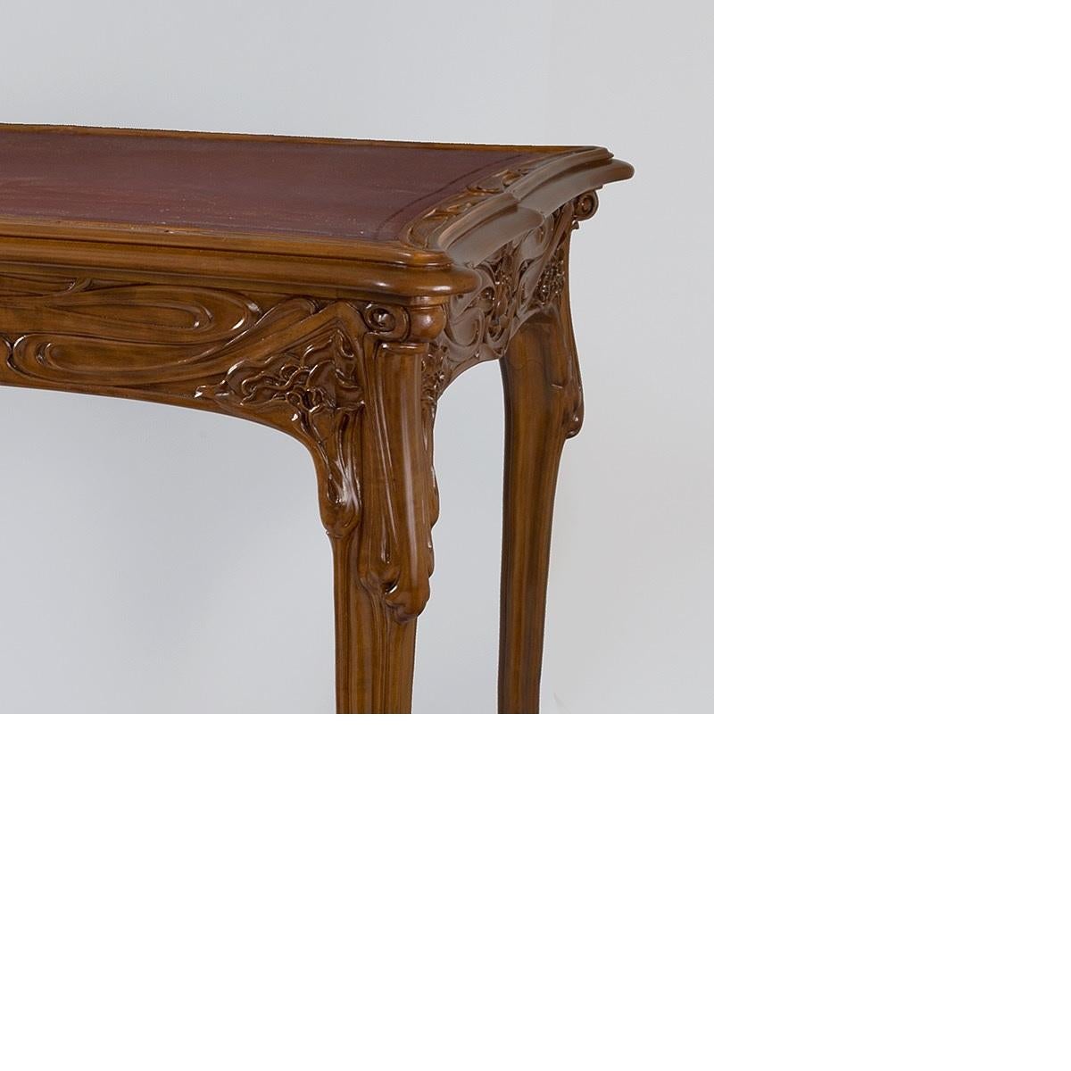 An exceptional French Art Nouveau fruitwood table attributed to Edouard Colonna with a black felt center, flanked by a scalloped decoration of vegetal carvings. The slightly curved legs adorn a rich decor of flowers and plants in relief, circa
