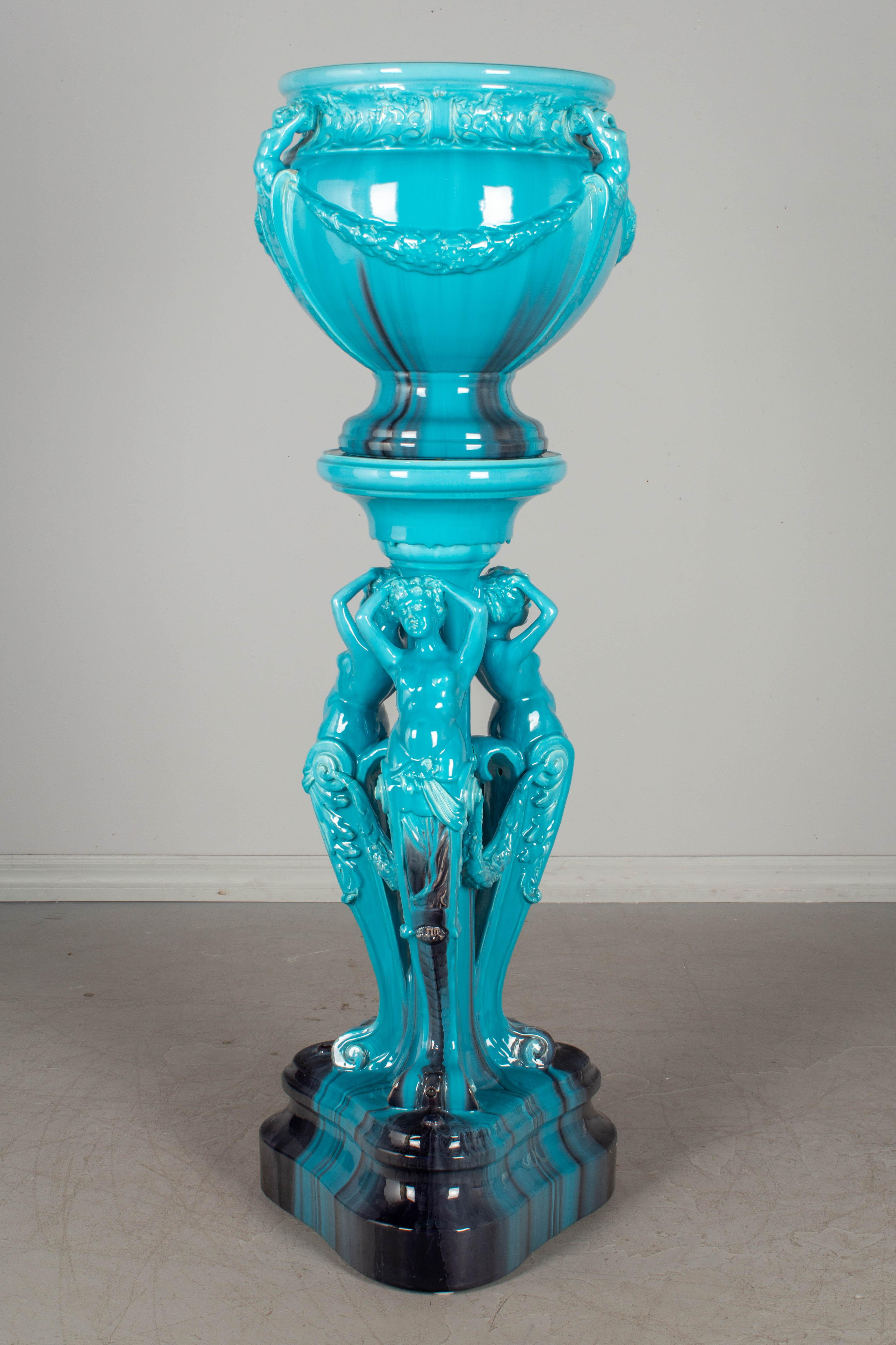 A French Art Nouveau Vallauris Majolica ceramic jardinière by Jerome Massier. Triangular pedestal base with three nude figures surmounted by a large bowl form planter with nudes and floral swags. Bright turquoise and deep purple glaze. In excellent