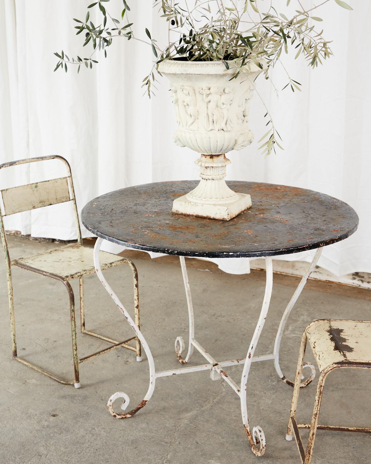 Painted French Art Nouveau period bistro table or garden dining table. The table features a patinated zinc top that is round supported by a scrolled wrought iron base. Full of character and charm with an aged finish on the painted surfaces. There is