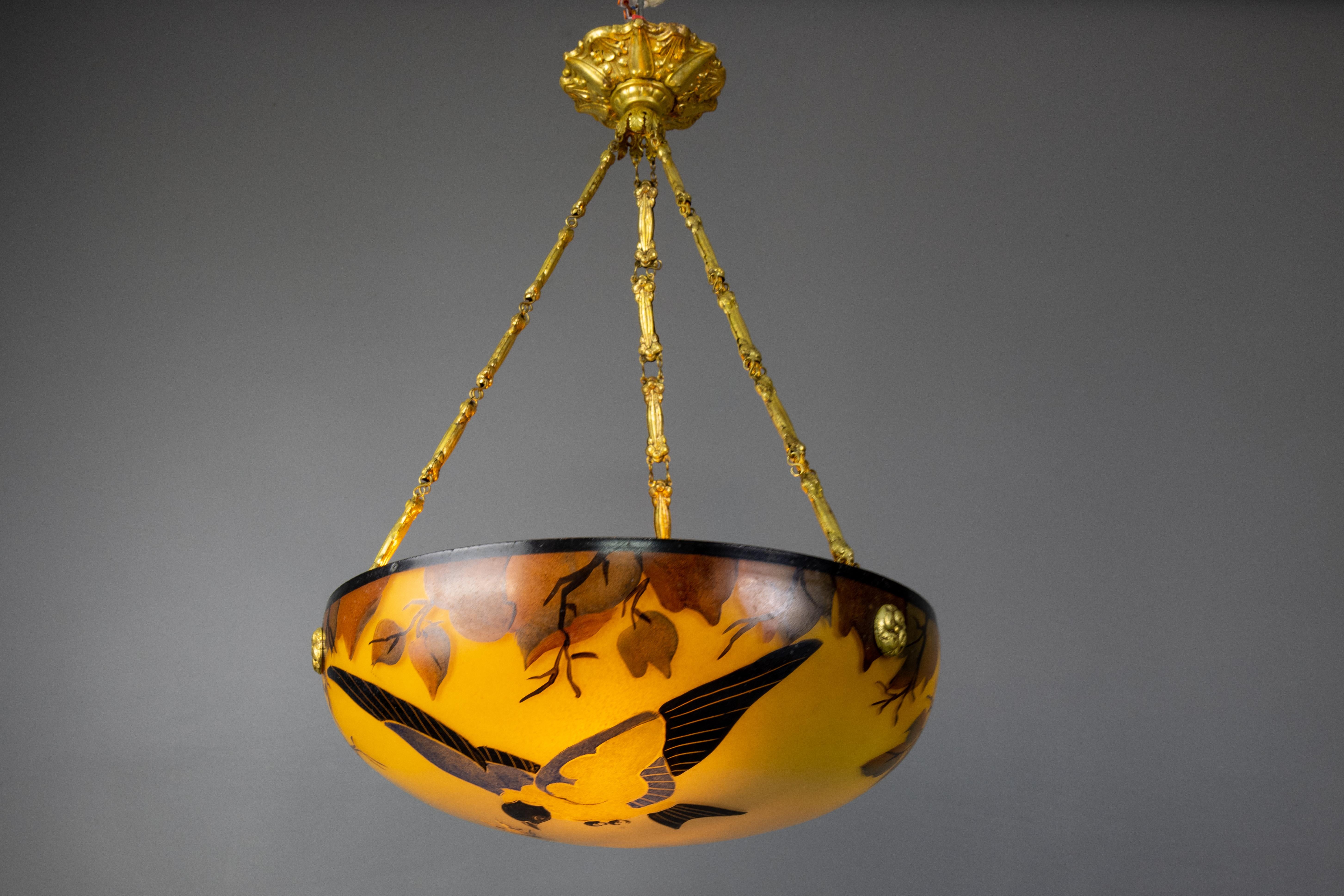 French Art Nouveau pendant light featuring yellow and brown glass with a bird motif, circa 1920.
This stunning Art Nouveau pendant light showcases a frosted glass bowl adorned with hand-painted stylized brown leaves, branches, and a bird capturing a
