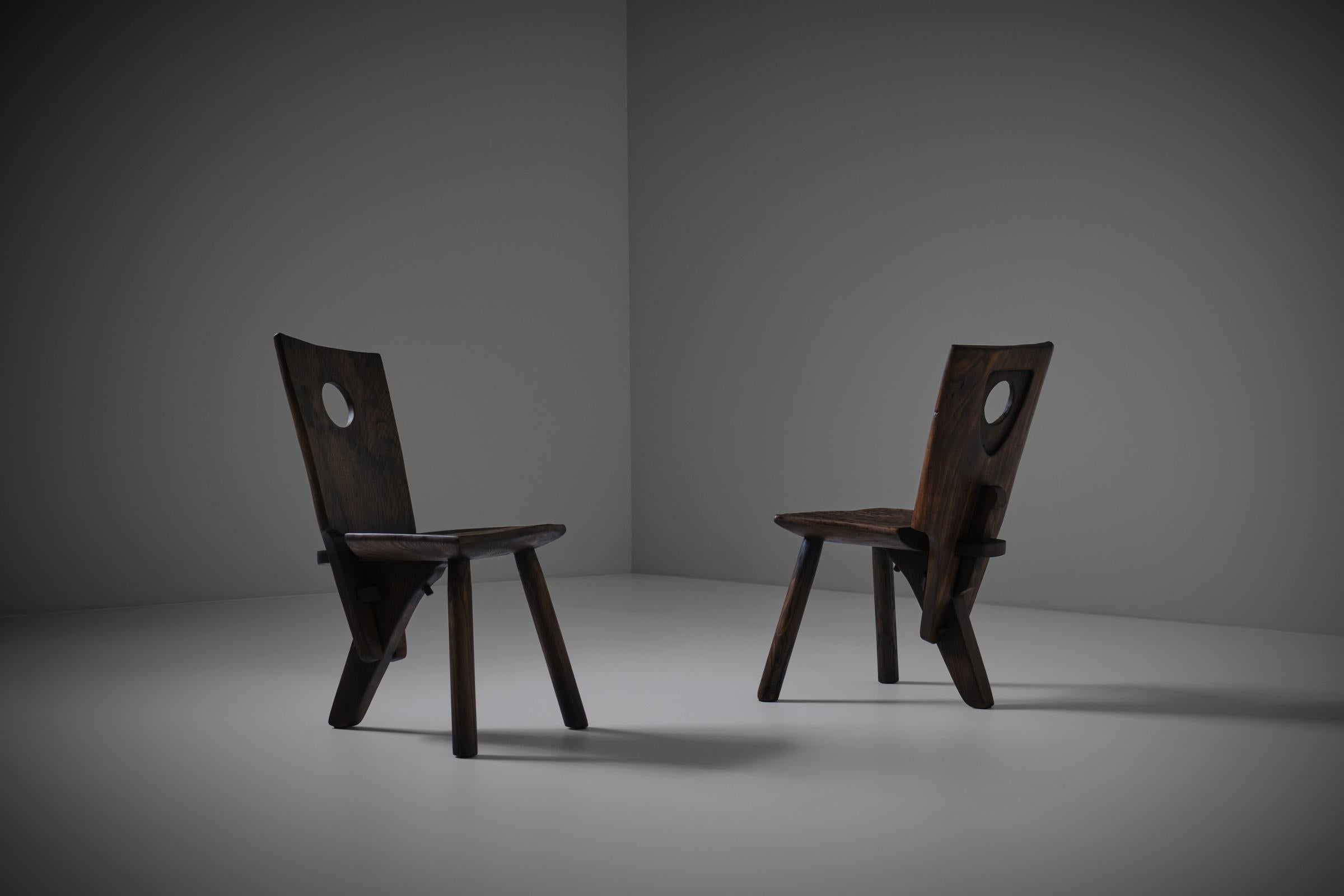 Solid elm wooden Art Populaire chairs, France 1960s. Beautiful primitive tripod chairs out of dark stained solid Elm wood. Interesting primitive authentic clamp construction resulting in a very sculptural appearance. The chairs shows many