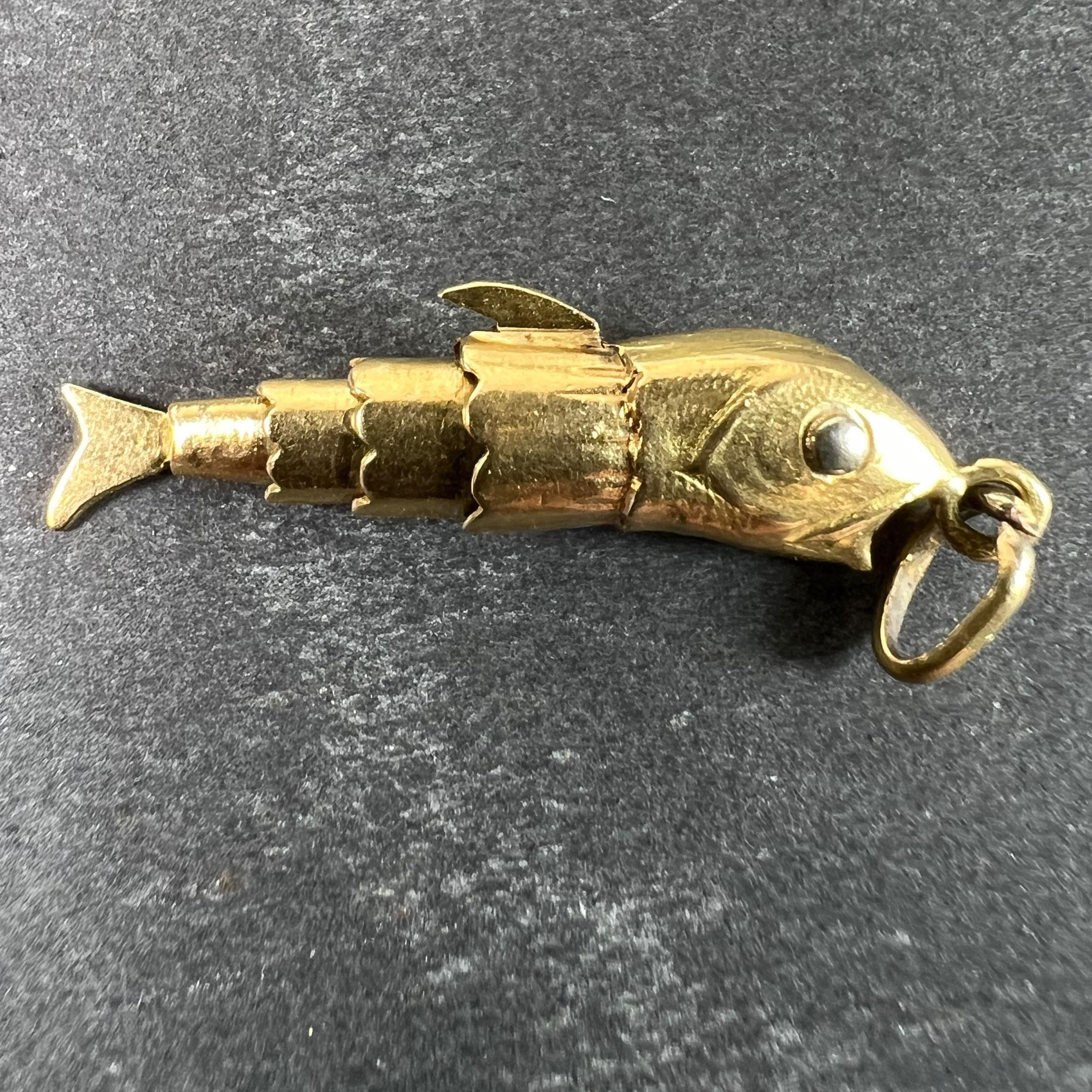 An 18 karat (18K) yellow French charm pendant designed as an articulated fish with moving body and tail, the eyes made of white gold. Stamped with the eagle's head for French manufacture and 18 karat gold along with an unknown maker's