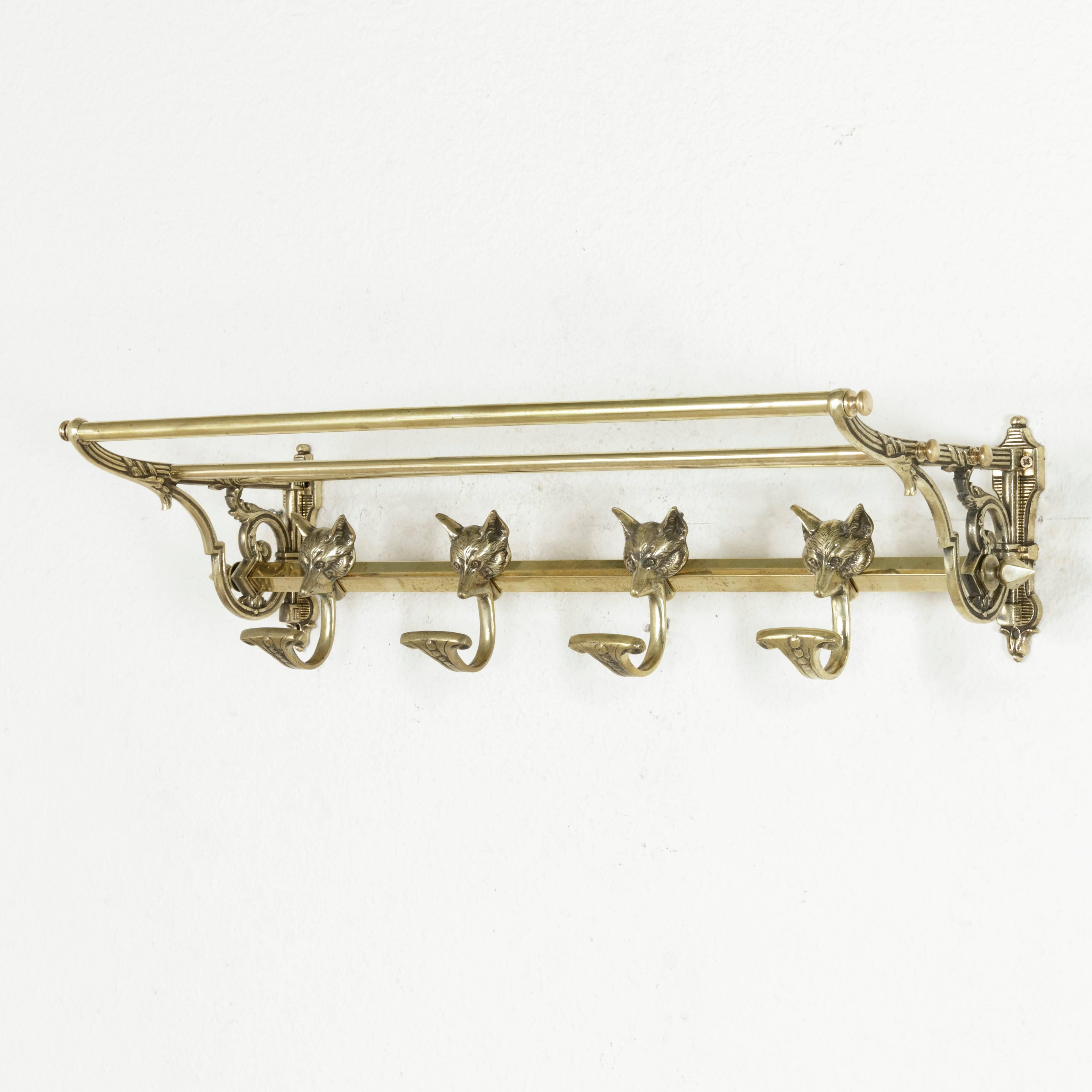 This French artisan-made cast brass hat and coat rack from the twentieth century features four sliding hooks topped with fox heads on the lower bar. Finials cap both ends of the bar and connect the support brackets. Extending from striated mounts,