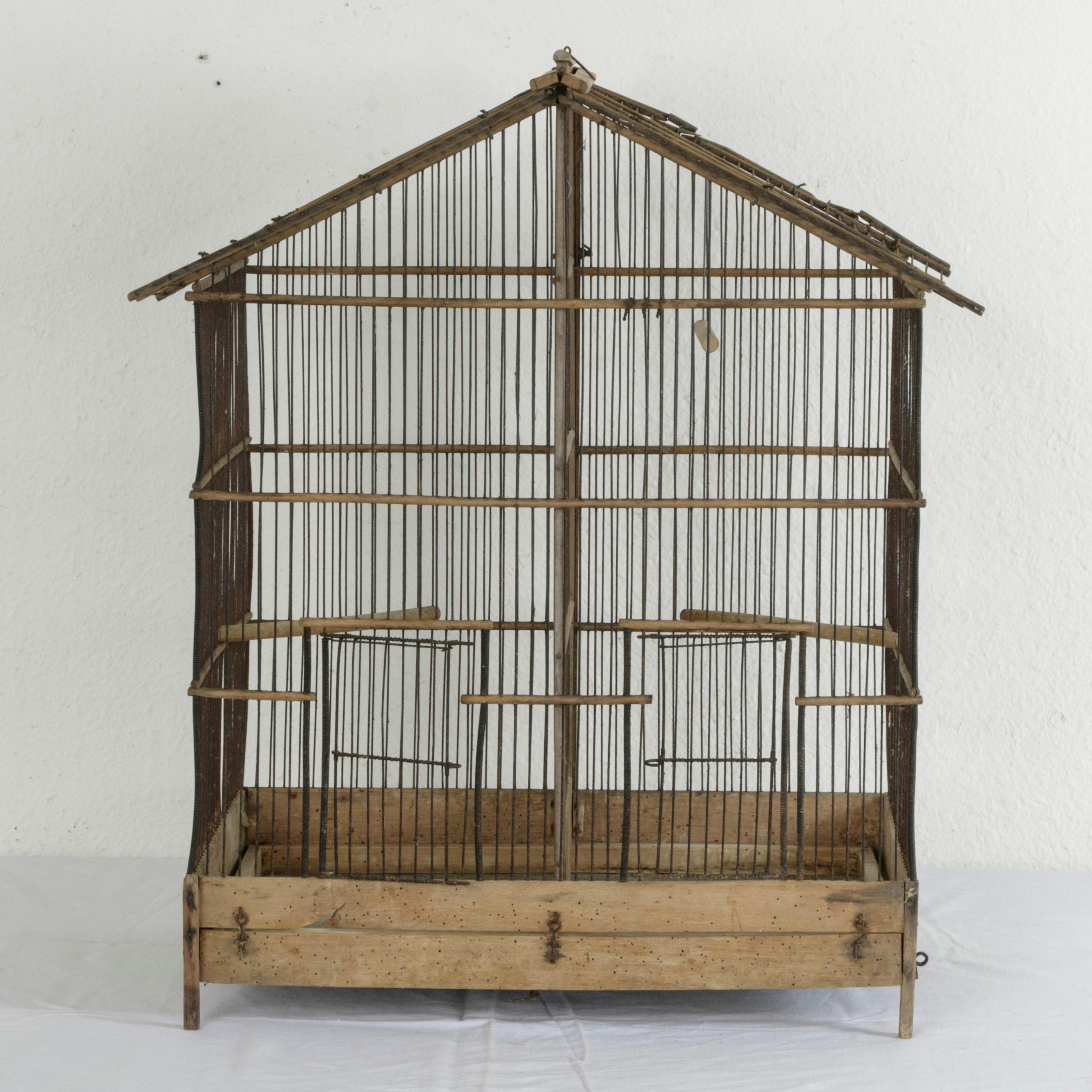 This artisan-made oak and wire bird cage takes the form of a gabled house and features a zinc bottom and three different perches. With two compartments that can be joined by removing the central wall, the cage has two hinged doors, one for each