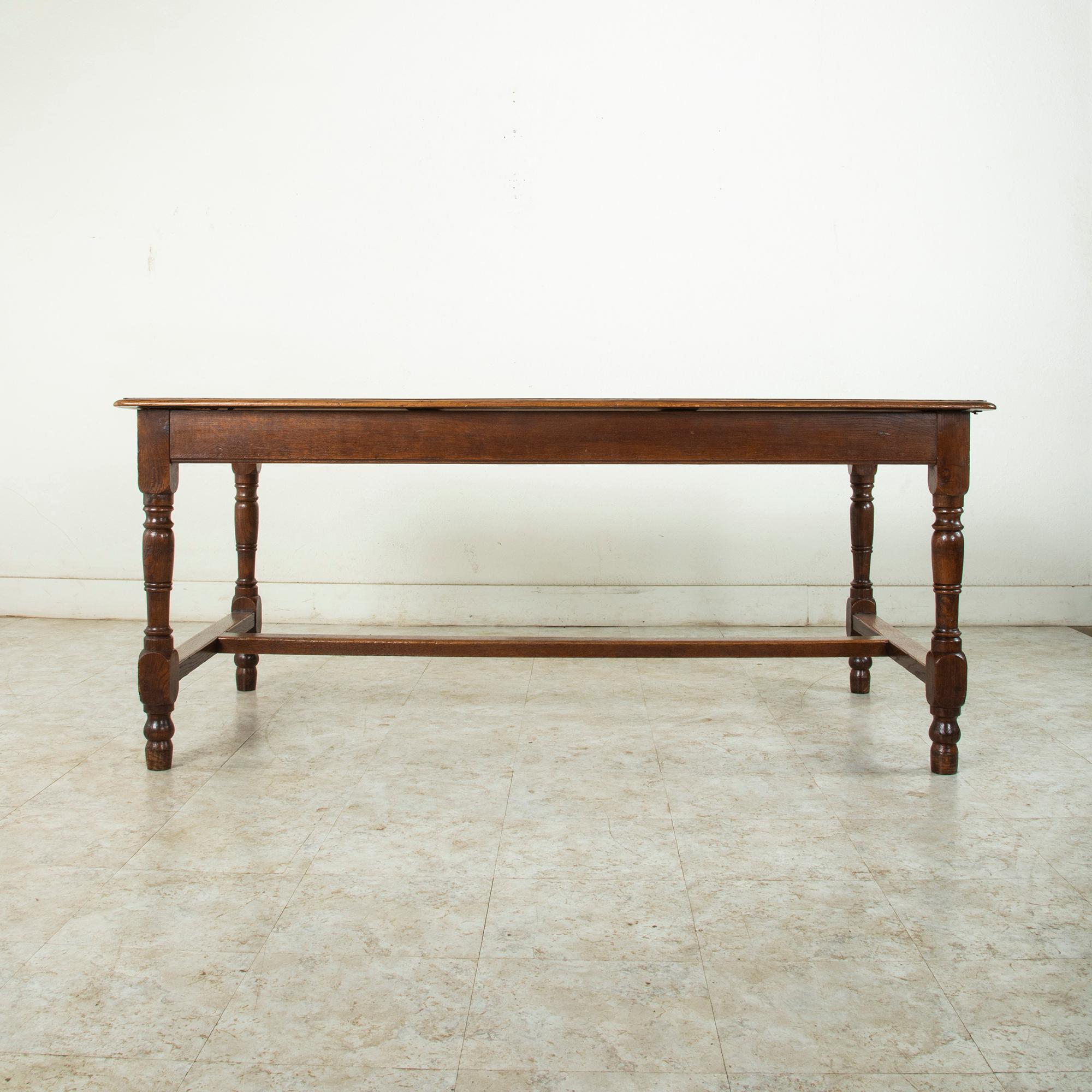 Found in Normandy, France, this French artisan made oak farm table or dining table from the turn of the 20th century features a beveled top constructed of six planks of wood. The top rests on turned legs joined by an H stretcher to provide