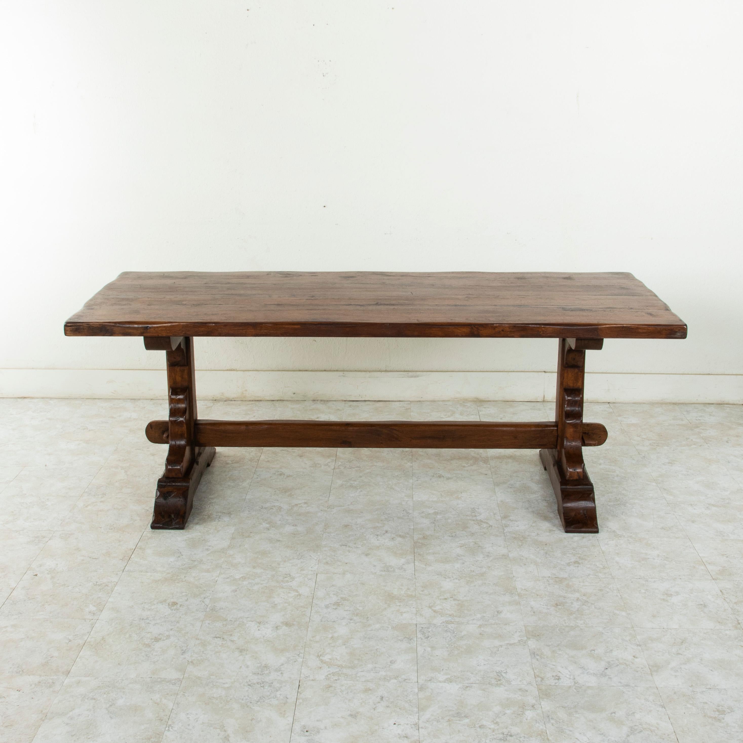 This circa 1930s monastery table or dining table is from the region of Normandy, France. Made of solid oak, this piece features a two inch thick top. Resting on a sturdy trestle base constructed using mortise and Tenon joinery and secured by oak
