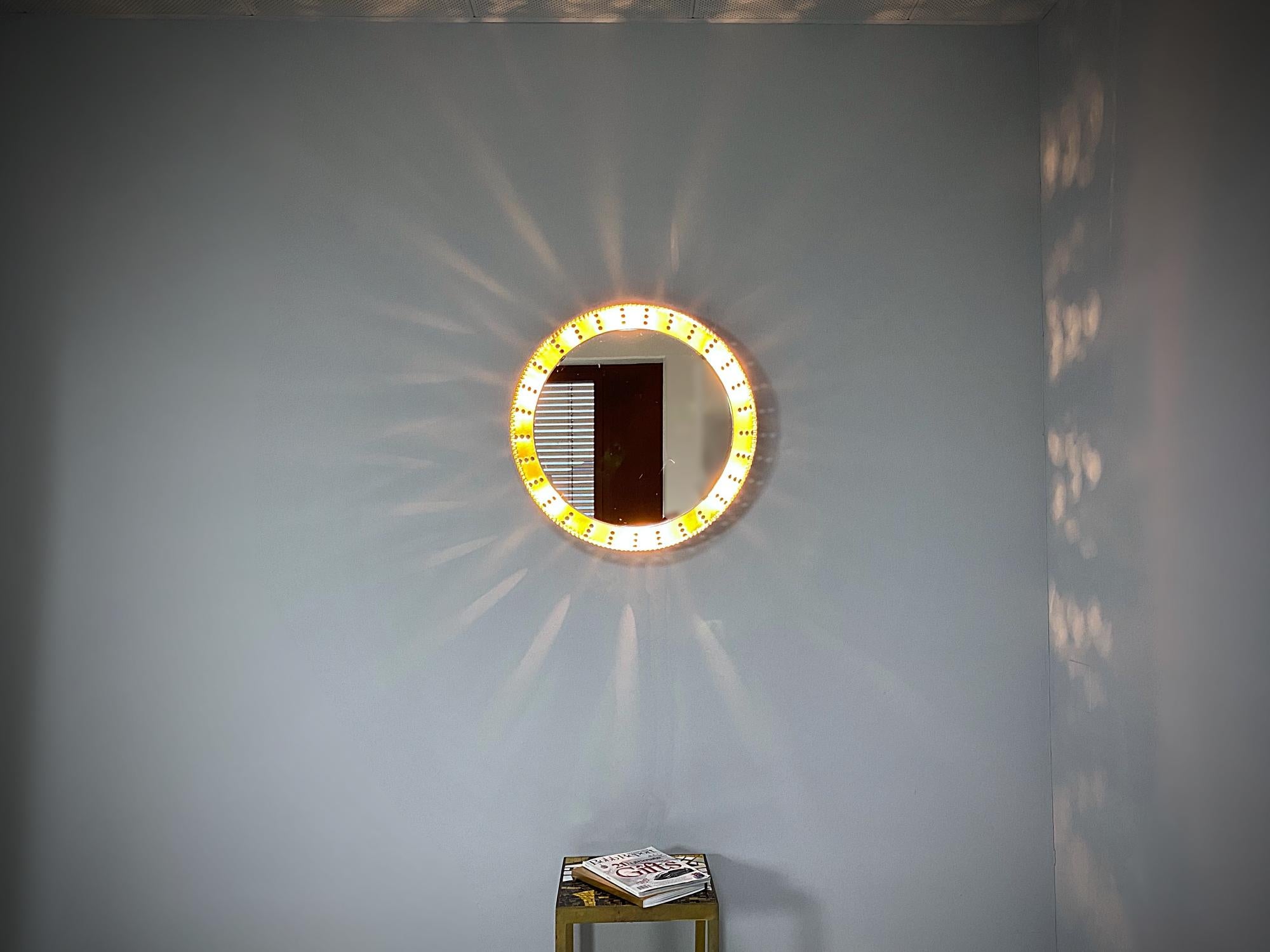 Miroir lumineux rond sculpté à la main avec cadre en métal laqué or, fabriqué dans les années 1960, France. Cadre massif avec bords festonnés décoratifs. Le miroir est en bon état avec quelques angles morts. Six douilles standard Edison E14.
Nous