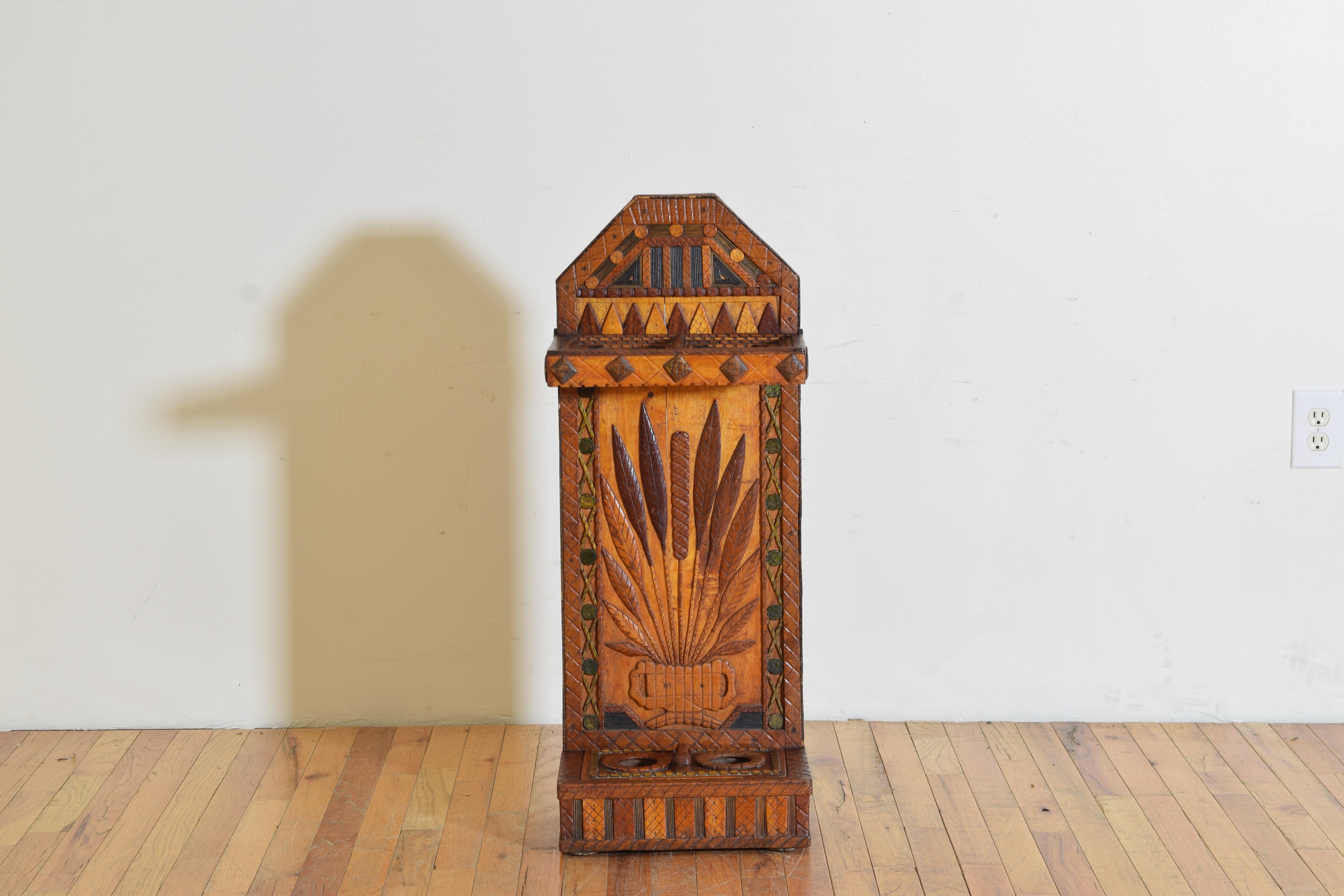 Uniquely shaped and expertly carved and painted this umbrella stand has an angular arched top with a double umbrella holder extending from the upper section, the main body decorated with stalks of wheat, the lower section having a removable