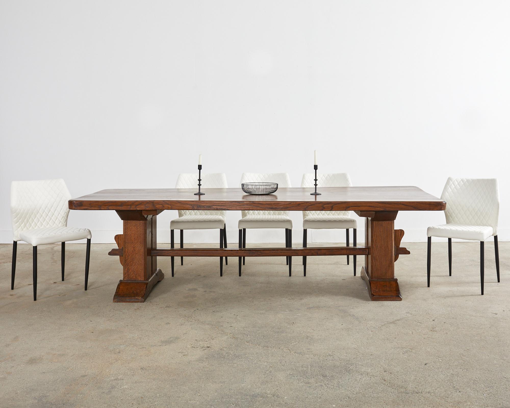 Substantial French decorative Arts & Crafts farmhouse dining table crafted from massive French oak timbers. The solid rectangular top is 2.5 inches thick and supported by a trestle base. The monumental legs are conjoined by a stretcher with exposed
