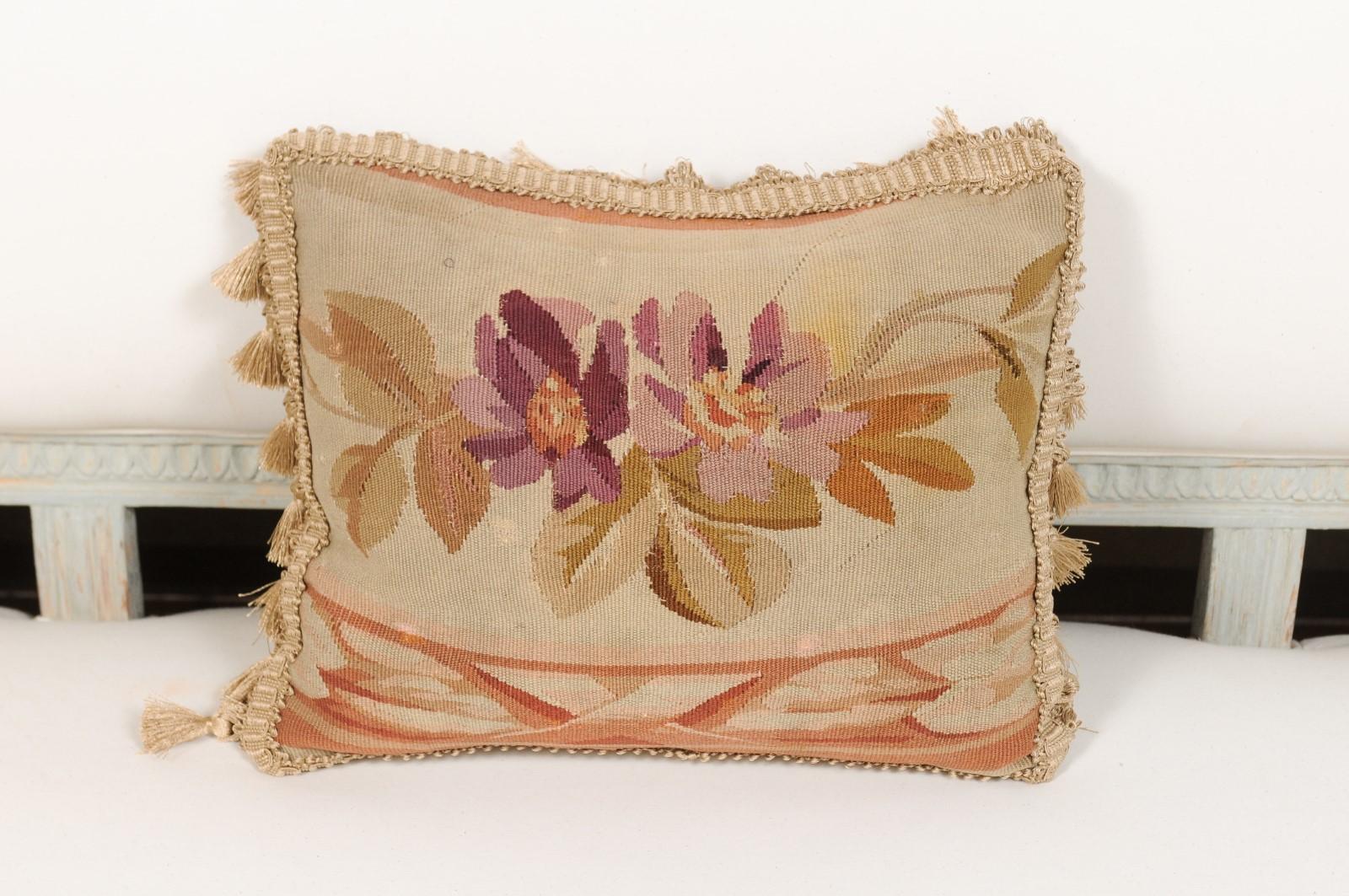 A French 19th century Aubusson tapestry pillow, with floral décor and tassels. Born during the 19th century in the Aubusson tapestry manufacture located in central France, this pillow features two delicate purple flowers, perfectly contrasted with