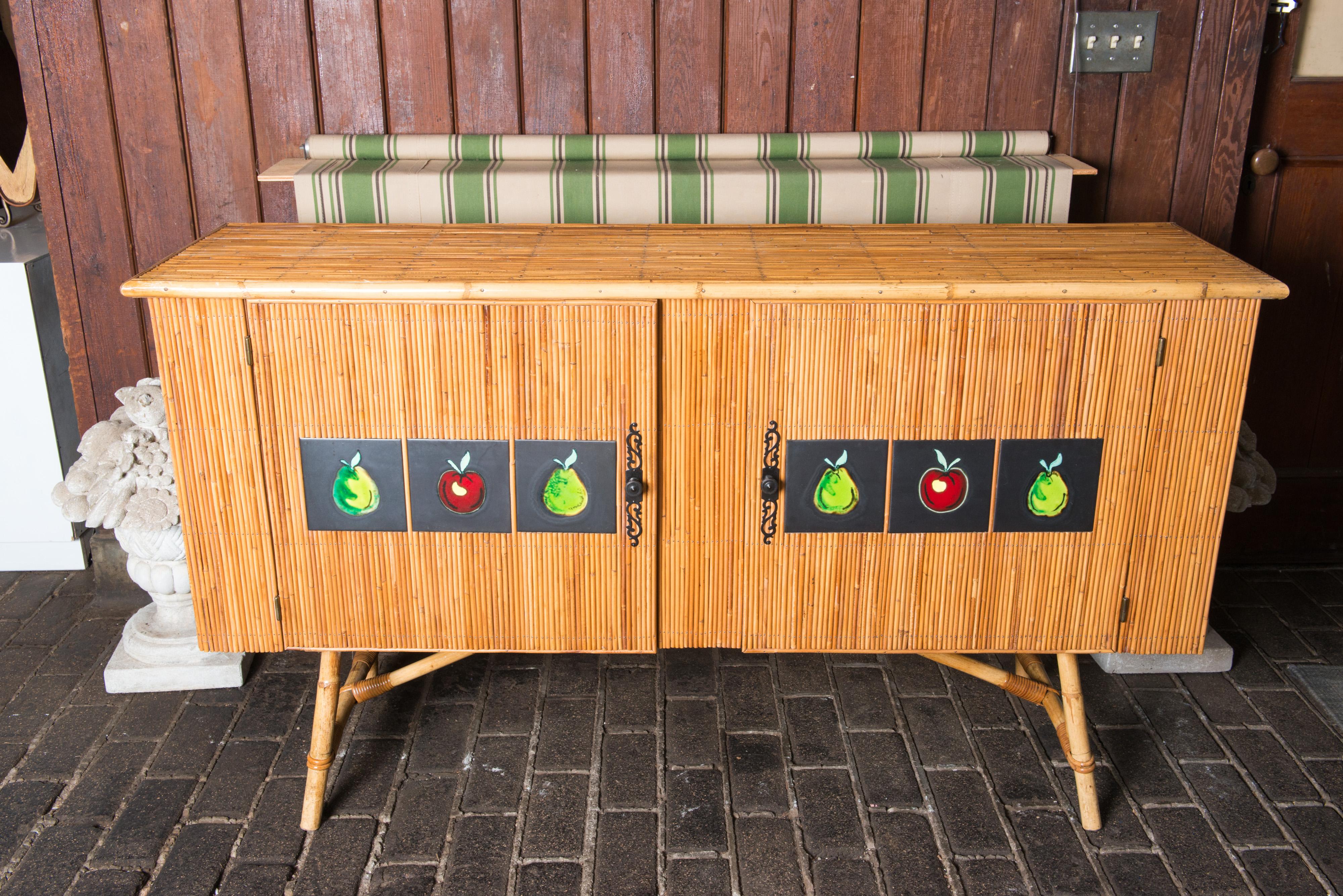 Beautiful and charming French 1950s split pencil bamboo sideboard by Adrien Audoux and Freida Minet. Six ceramic tiles of apples and pears by artist, Colette Gueden punctuate the two doors. The buffet interior consists 
of a shelf behind each door.