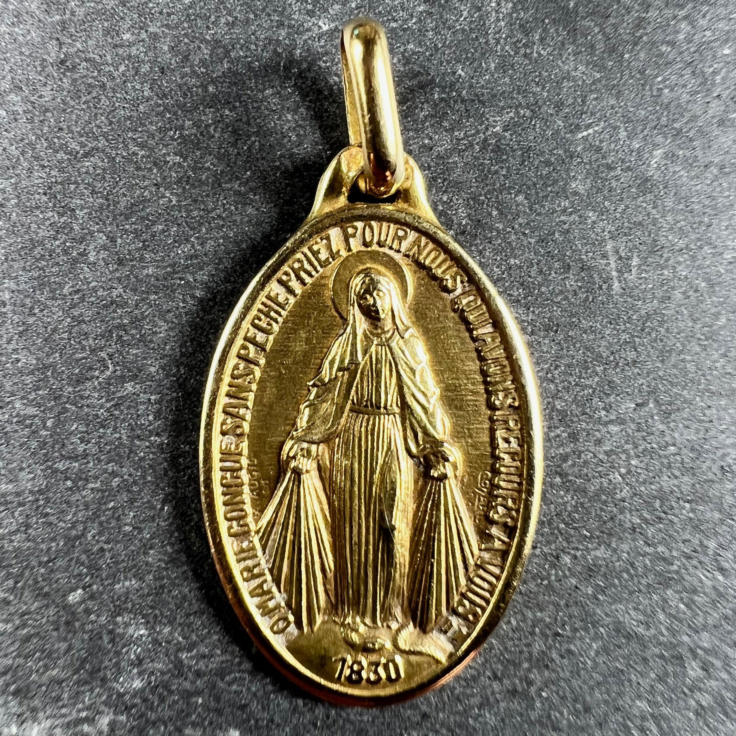 A French 18 karat (18K) yellow gold charm pendant designed as the Miraculous Medal by Augis. The medal depicts the Virgin Mary standing on a globe above the date 1830, crushing a serpent beneath her feet with rays shooting from her hands to