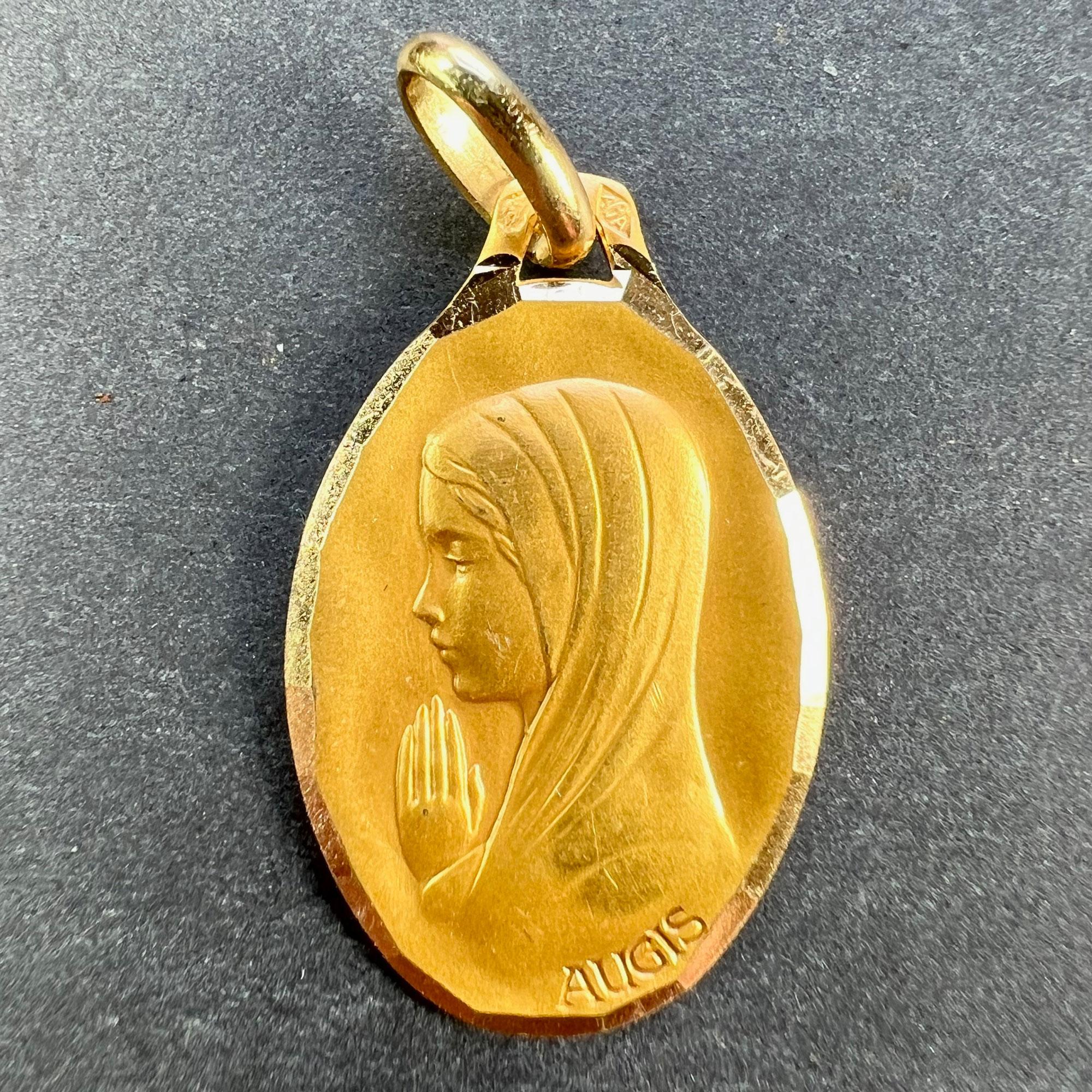 Pendentif français en or jaune 18 carats (18K) conçu comme une médaille ovale représentant la Vierge Marie dans un cadre à facettes. Signé Augis. Estampillé de la tête d'aigle pour la fabrication française et de l'or 18 carats, avec la marque