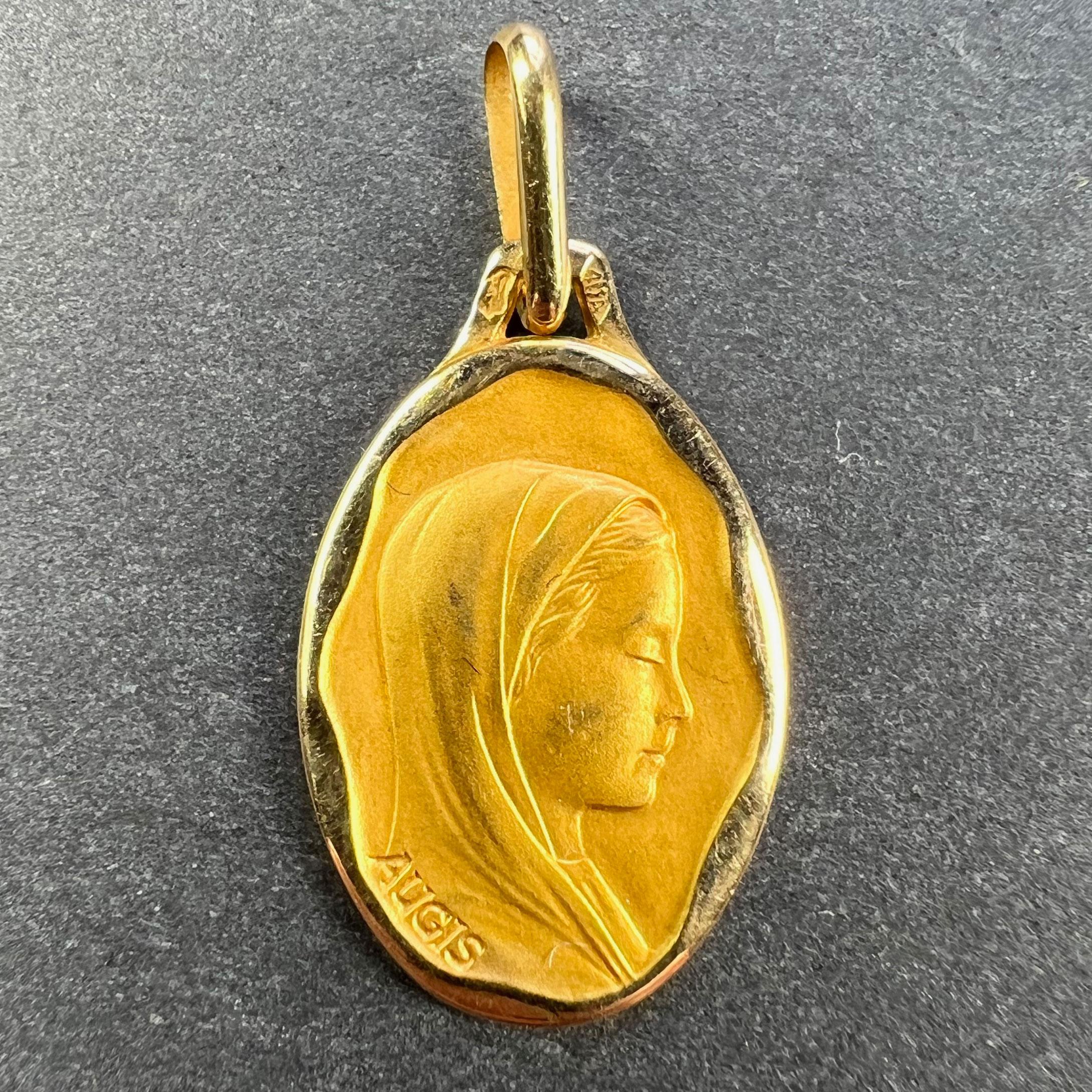 A French 18 karat (18K) yellow gold pendant designed as an oval medal depicting the Virgin Mary within a wavy polished frame. Signed Augis. Stamped with the eagle’s head for French manufacture and 18 karat gold, with maker’s mark for