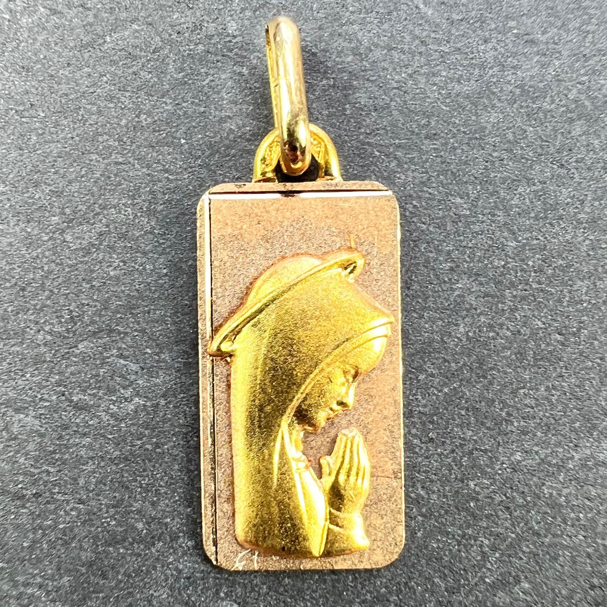 A French 18 karat (18K) yellow gold pendant designed as a rectangular medal depicting the Virgin Mary within a halo on a rose gold background. Marked with an A for Augis to the reverse of the pendant loop. Stamped with the eagle’s head for French