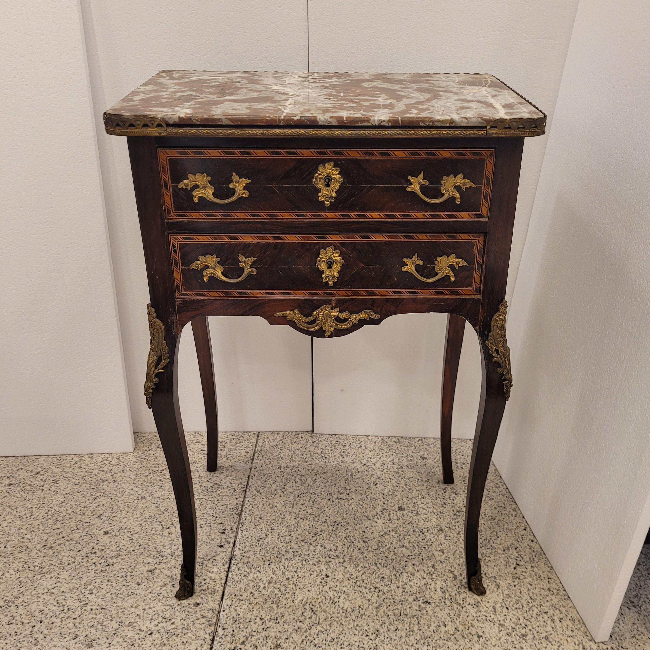 Questa splendida cassettiera francese di piccole dimensioni è realizzata in stile Luigi XV, periodo Napoleone III. Presenta un imponente piano in marmo color ocra con intarsi grigi e perlati, con un profilo in ottone dorato come balaustra traforata.