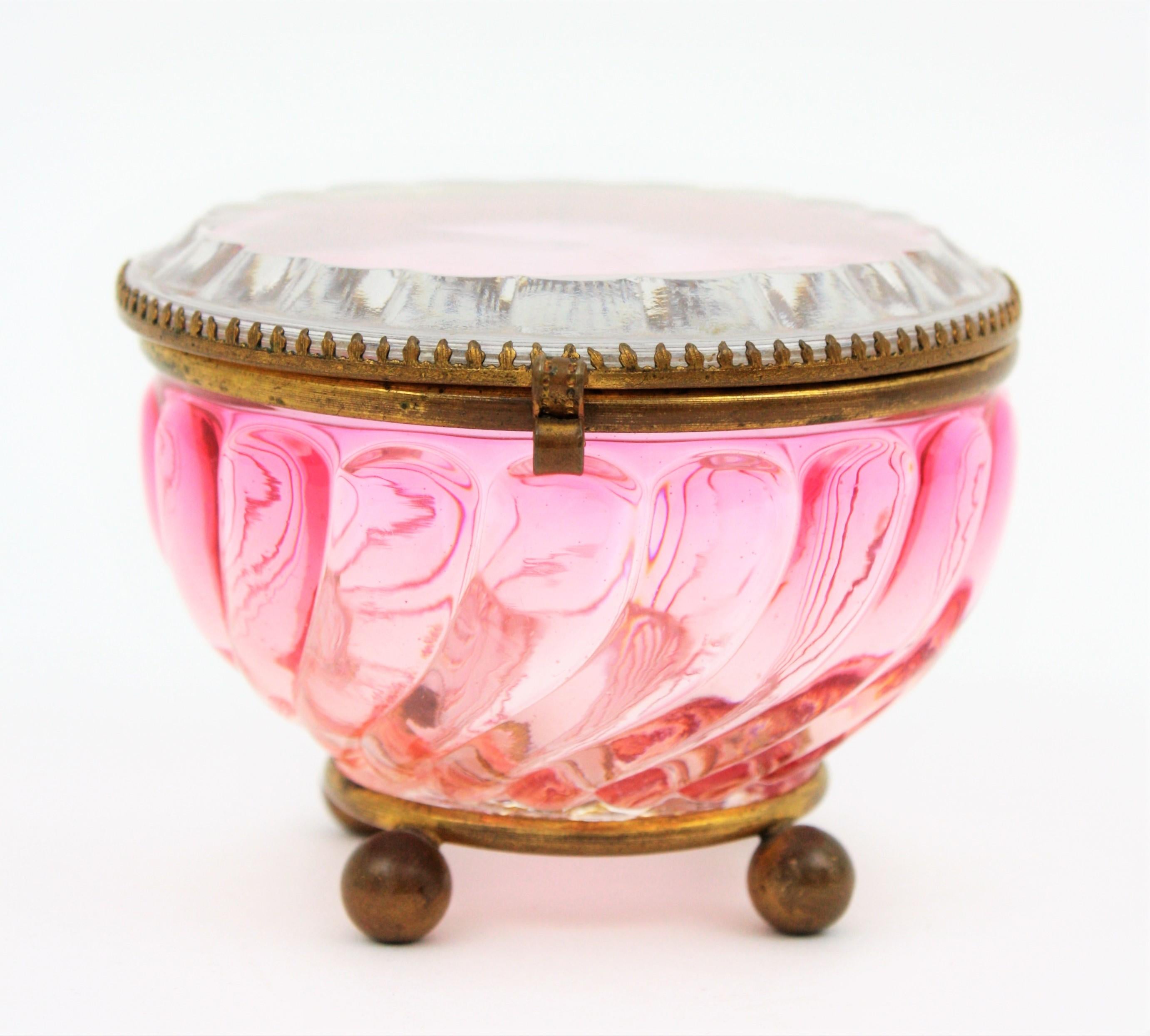 Exquisite Rose Teinte Amberina swirl jewelry box with brass details by Baccarat. France, 1920-1930s.
This lovely signed Baccarat crystal jewelry box in the Amberina Rose Teinte Swirled Bamboo patten features on a four-ball brass feet and it has an