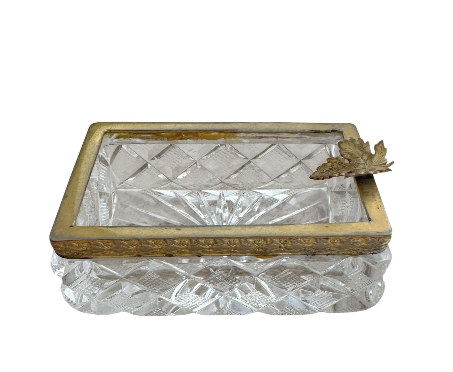 Cendrier ou attrape-tout sophistiqué en cristal français dans le style de Baccarat, présentant une forme rectangulaire remarquable, fabriquée à partir de cristal épais et facetté. La partie supérieure est encadrée d'un bord en bronze doré, ce qui